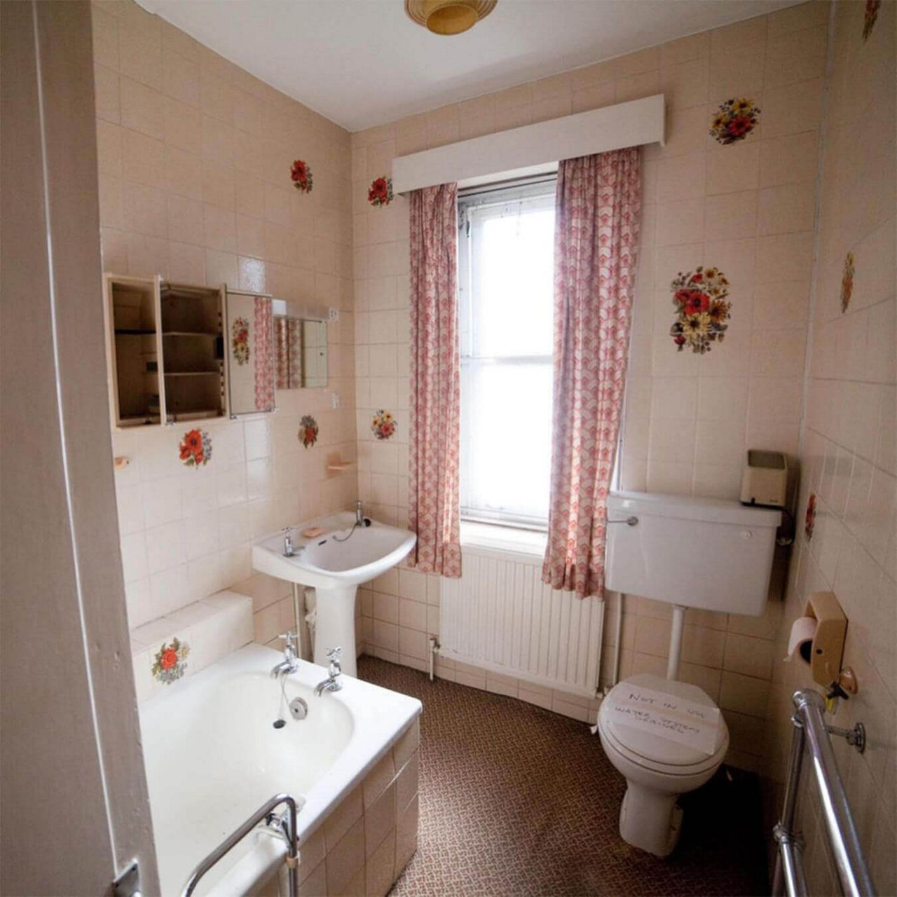 A before picture of @restorationcouple's bathroom with floral wall tiles, vintage style toilet, sink and bathtub and a large window.