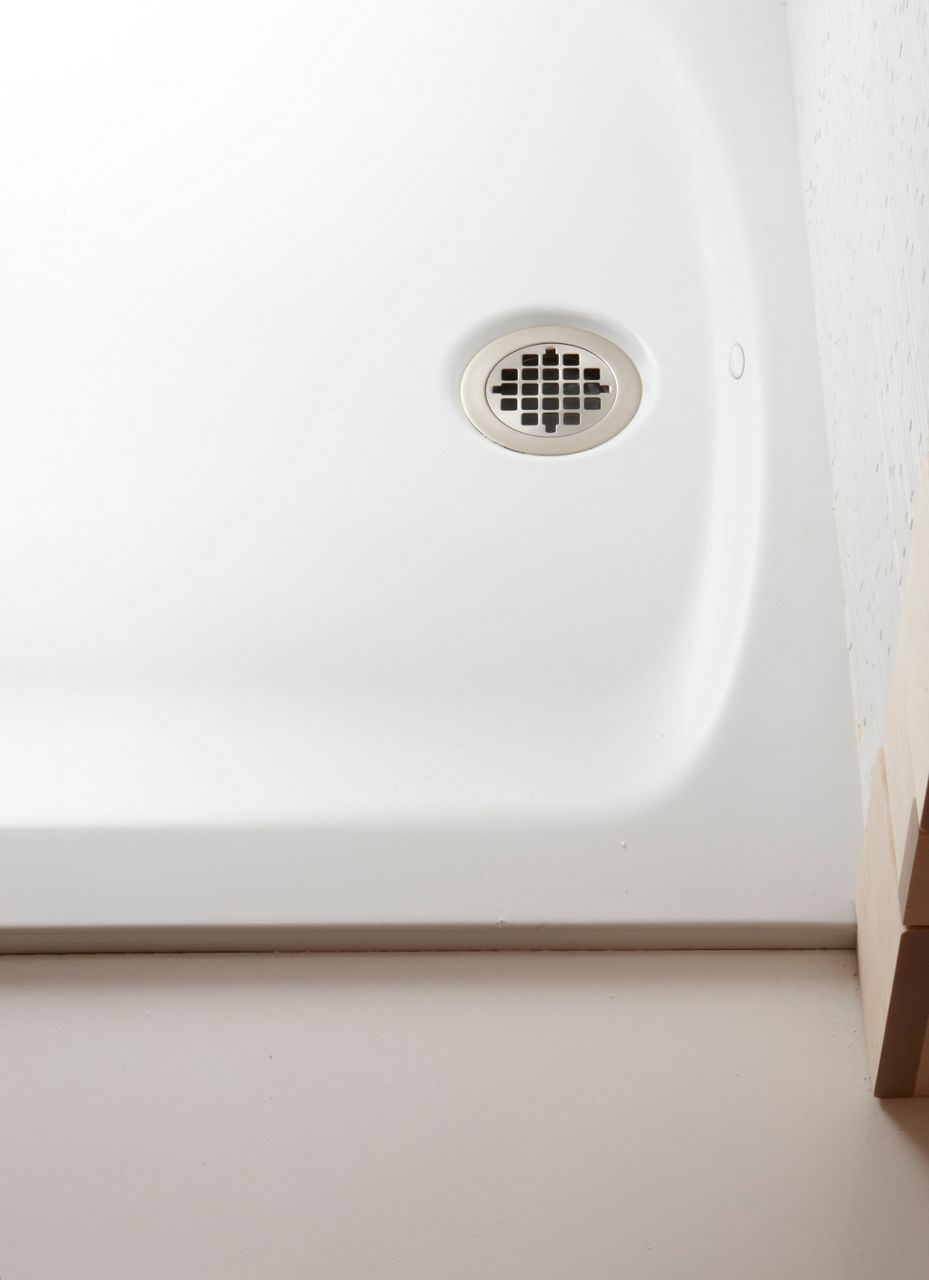 Close-up of a white surface with a circular, grid-patterned metal drain cover, embedded within the smooth material.