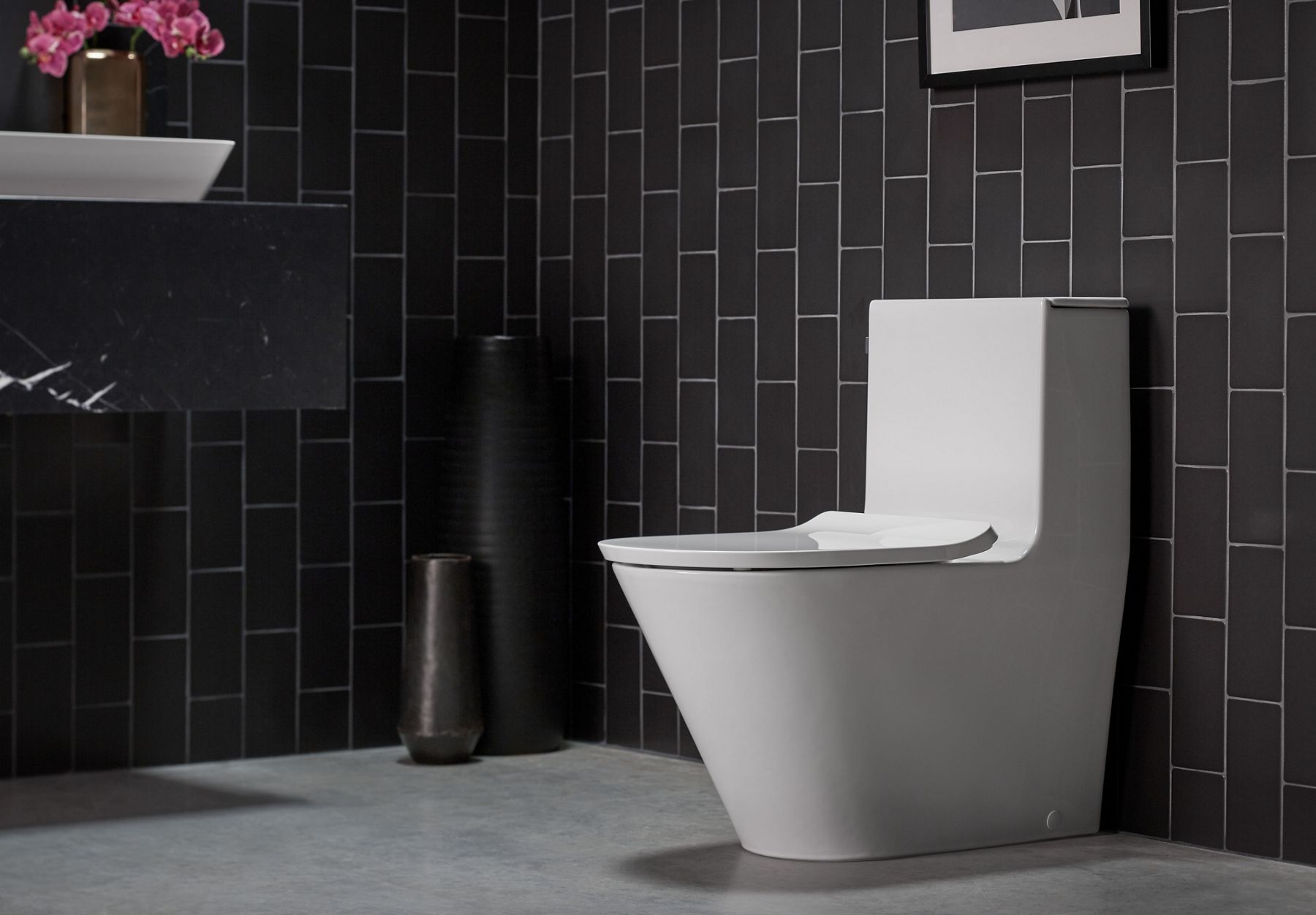 A contemporary white toilet against a black tile wall.