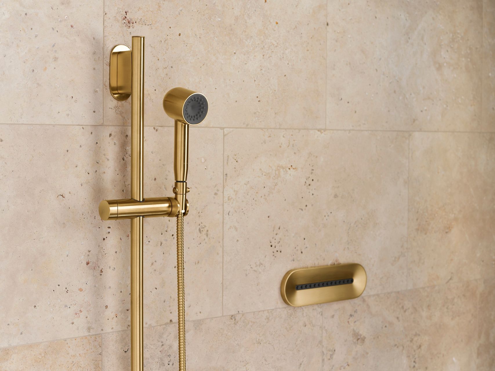 A brushed brass handshower on a tan stone wall.