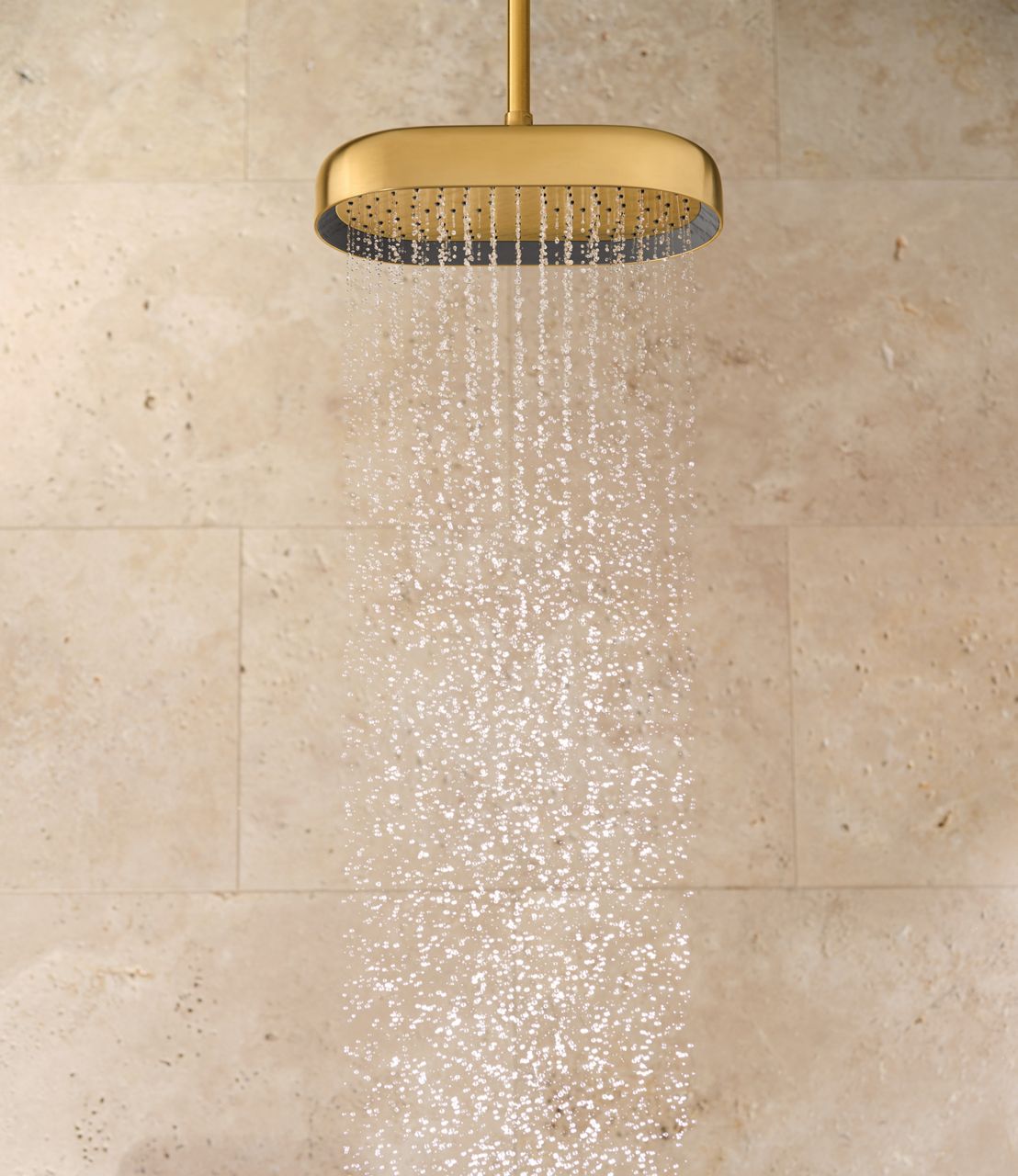 Close-up of a luxurious gold rain showerhead mounted on a beige stone wall, with water cascading evenly from multiple small nozzles, creating a soothing waterfall effect.