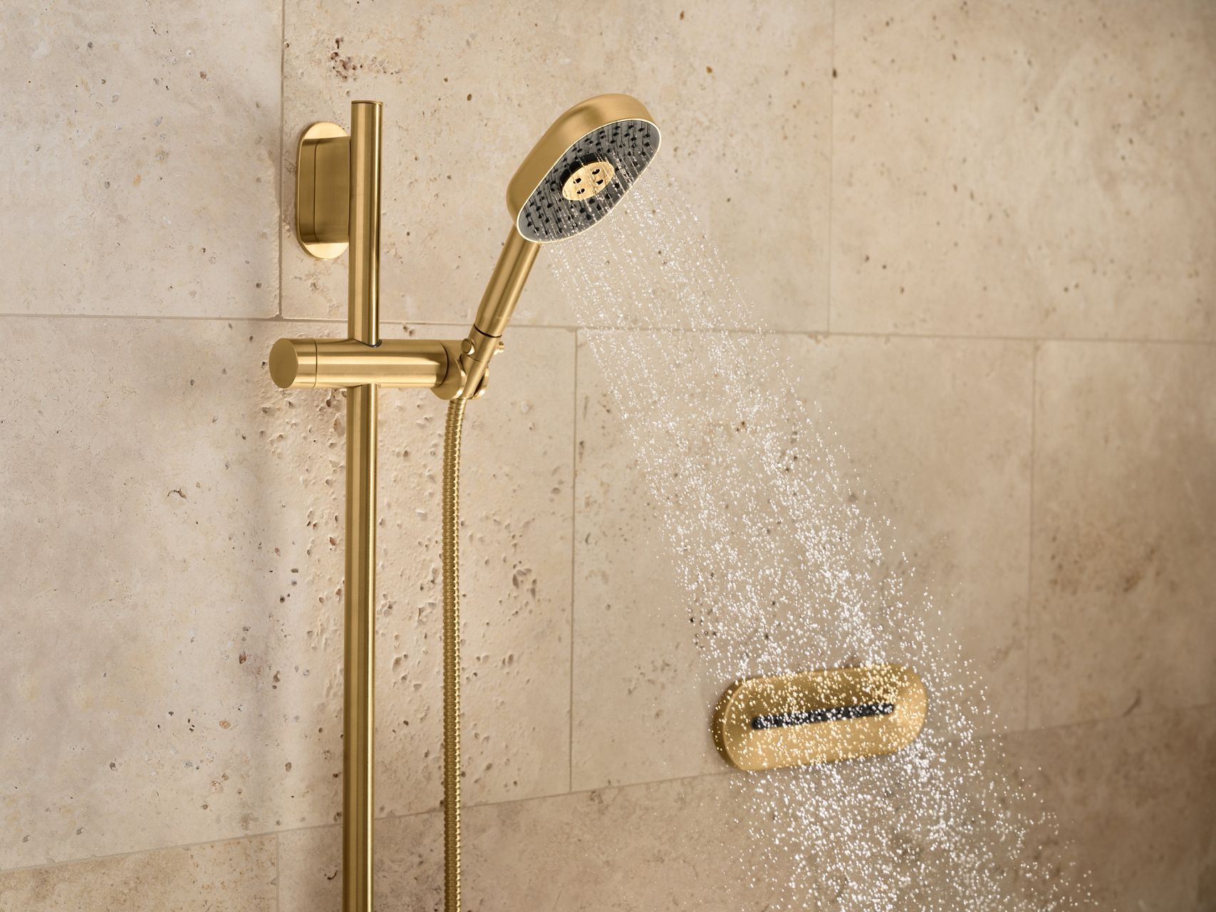 Close-up of a gold-colored adjustable shower rail with a handheld showerhead mounted on a beige textured tile wall.
