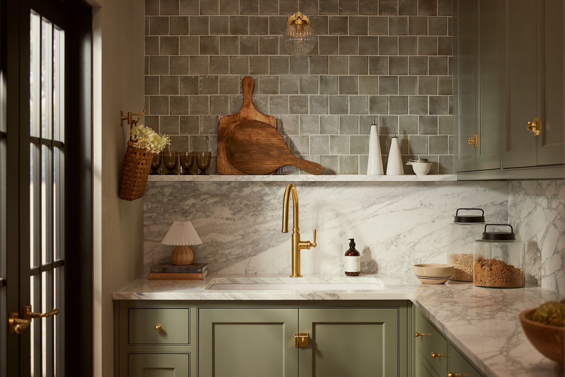 Edalyn™ kitchen faucet installed at a modern sink beneath a window, featuring a high-arc pull-down design with a refined brass finish.