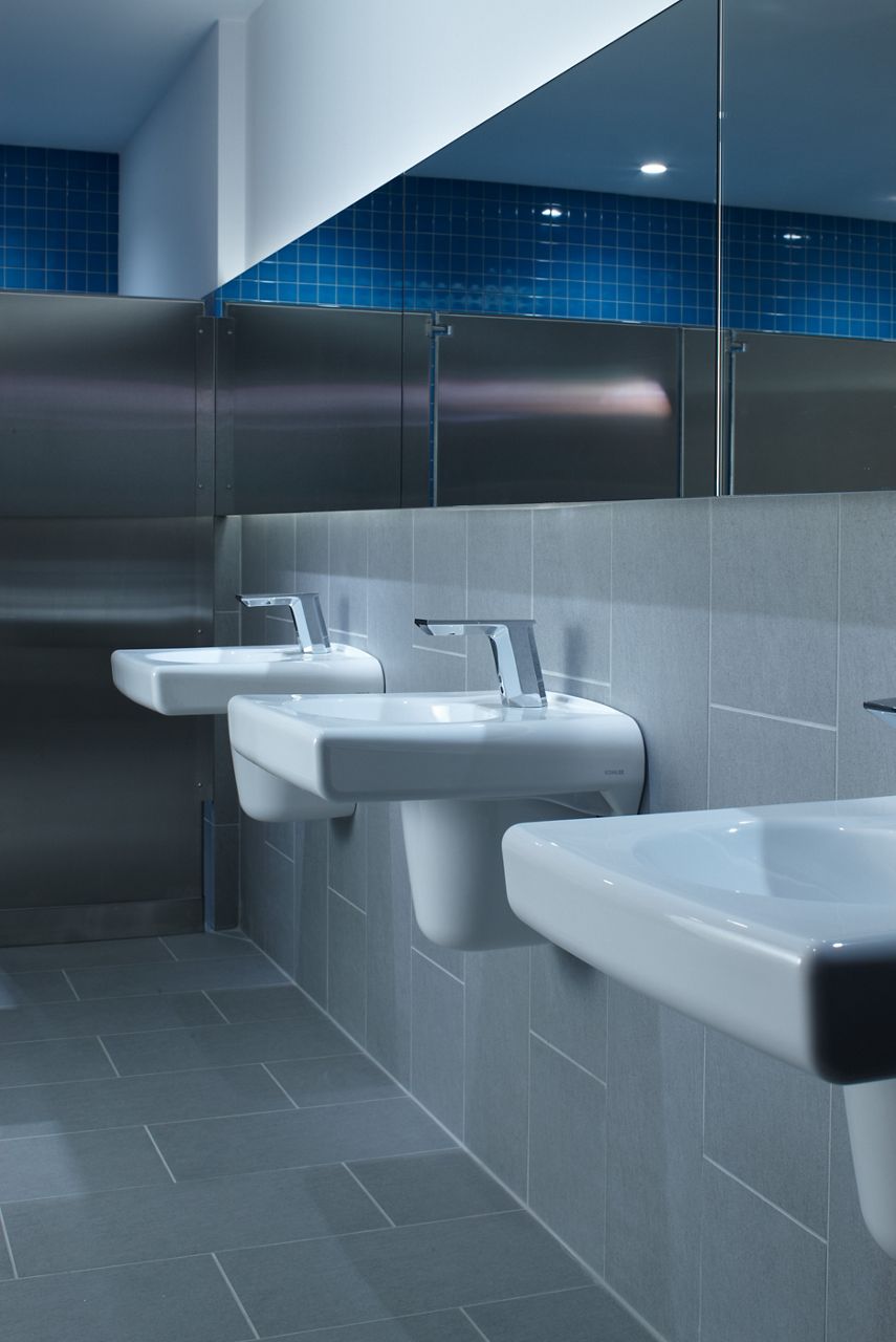 A line-up of three wall-mount sinks with contemporary faucets against a gray tile wall.