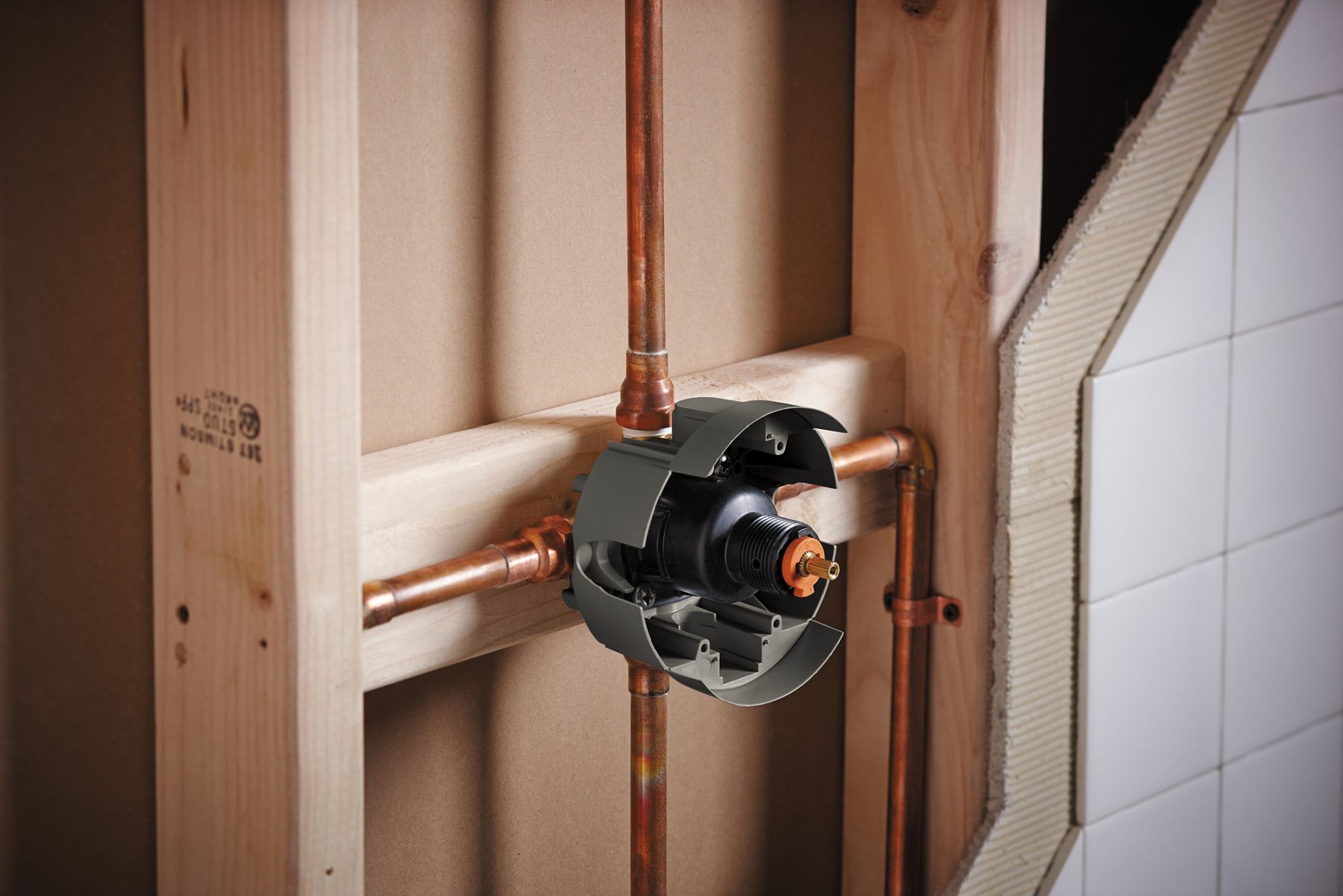 An exposed shower valve attached to wood framing with copper pipes connecting to it on four sides.