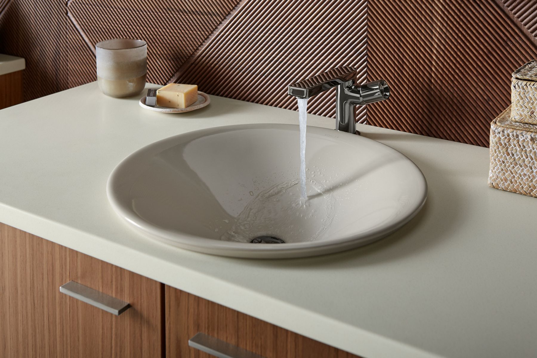 A round beige bathroom sink with a contemporary faucet pouring water into it.