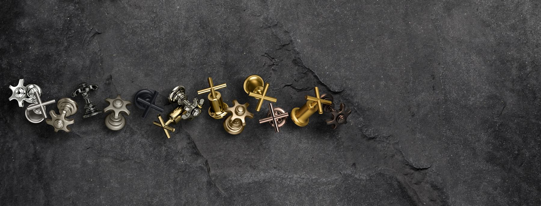 Several faucet handles in various finishes laying on a dark gray surface.