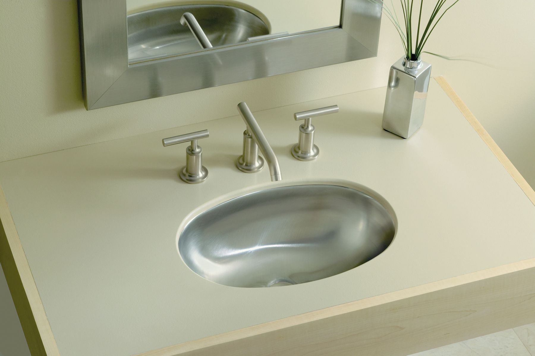 An overhead view of a chrome bathroom sink faucet with and undermount stainless steel sink, backed by a mirror