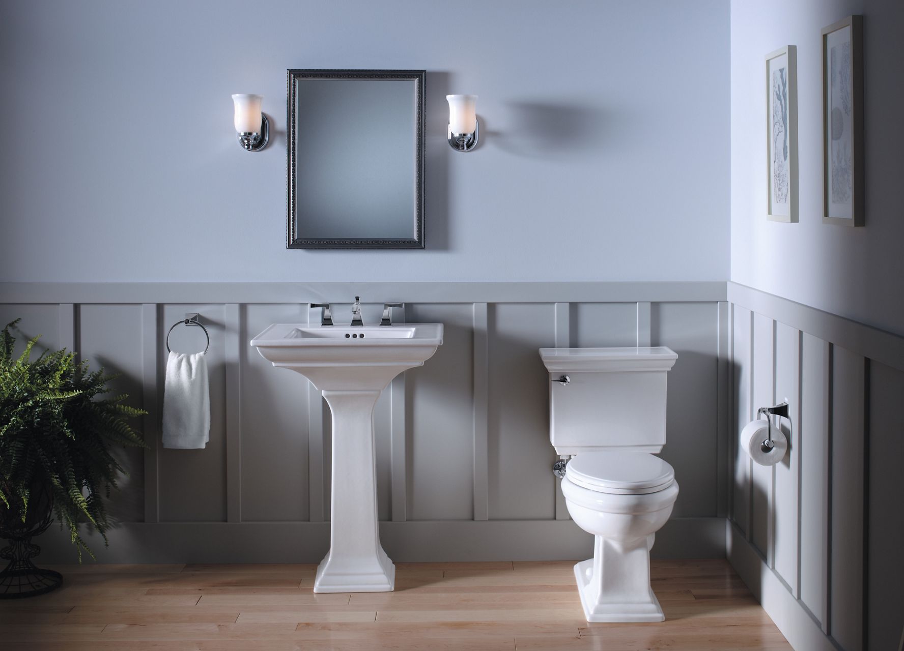 A calm, white bathroom with large format hex tile floors, wainscotted alcove with white KOHLER Memoirs® toilet, and a vase of white flowers on a small round table.