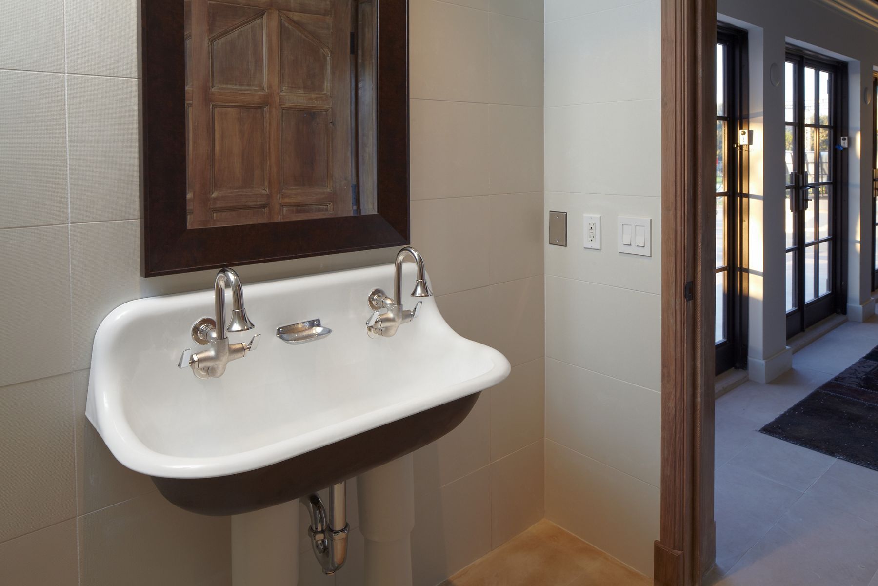 A cast iron trough sink with a white enameled interior and black exterior, mounted to a tan wall.