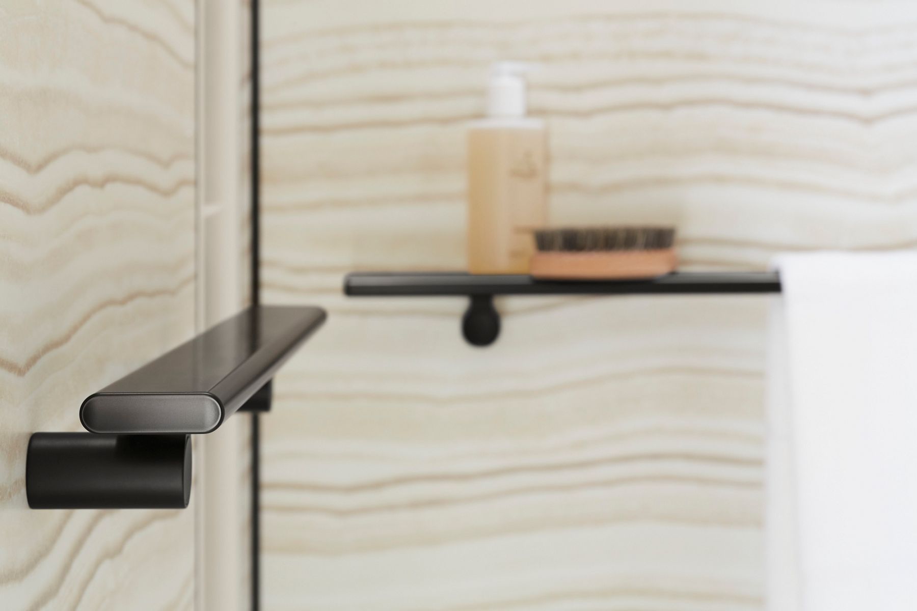 A close-up side view of a black shower shelf and a black shower shelf with a bottle of soup in the background