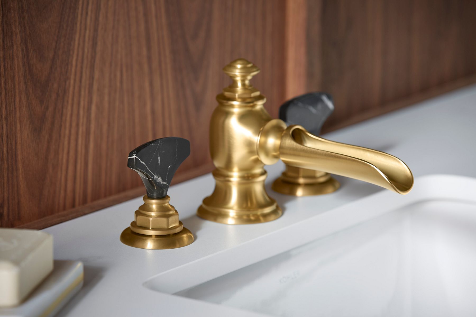 A close-up of a gold bathroom sink faucet and semiprecious stone faucet lever handle with a gold base