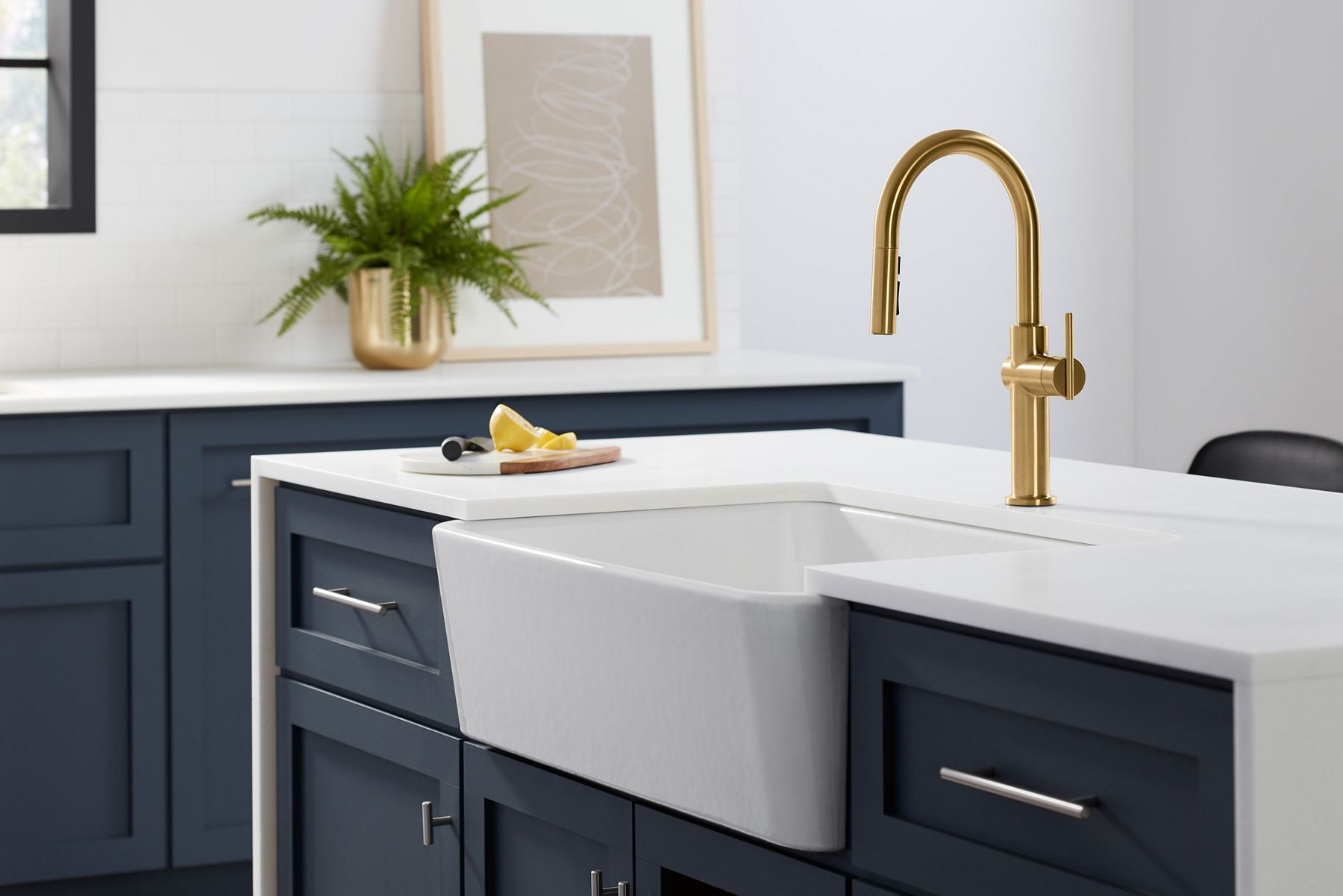 A white farmhouse sink in a kitchen island with dark blue cabinets and a white counter top