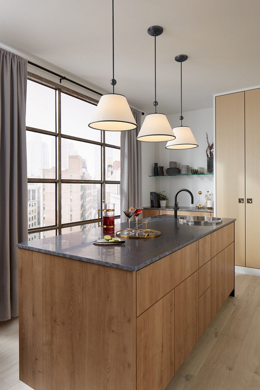 Three Parohn one-light pendants in Gunmetal finish above the island of a contemporary kitchen overlooking a city scape through a large window.