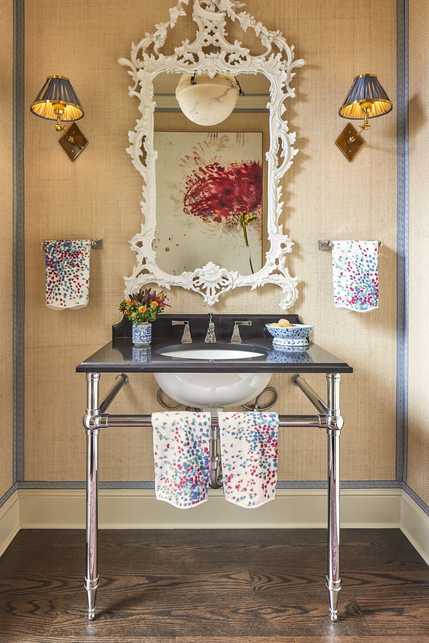 A vanity space with a console table sink with polished chrome legs and an ornate mirror with an intricate white frame against a soft yellow wall.