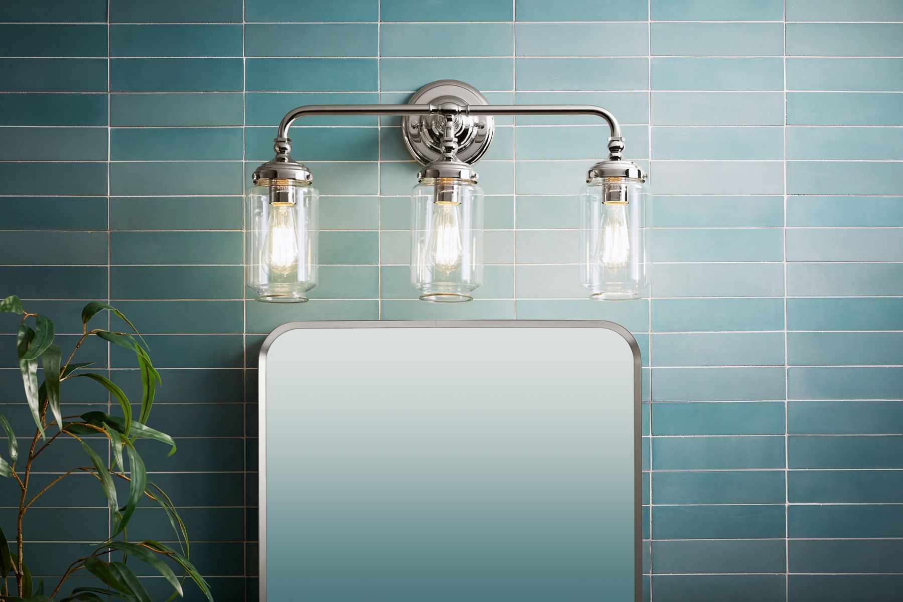 An Artifacts three-light sconce in Polished Chrome above a mirror with a light-blue tiled wall.