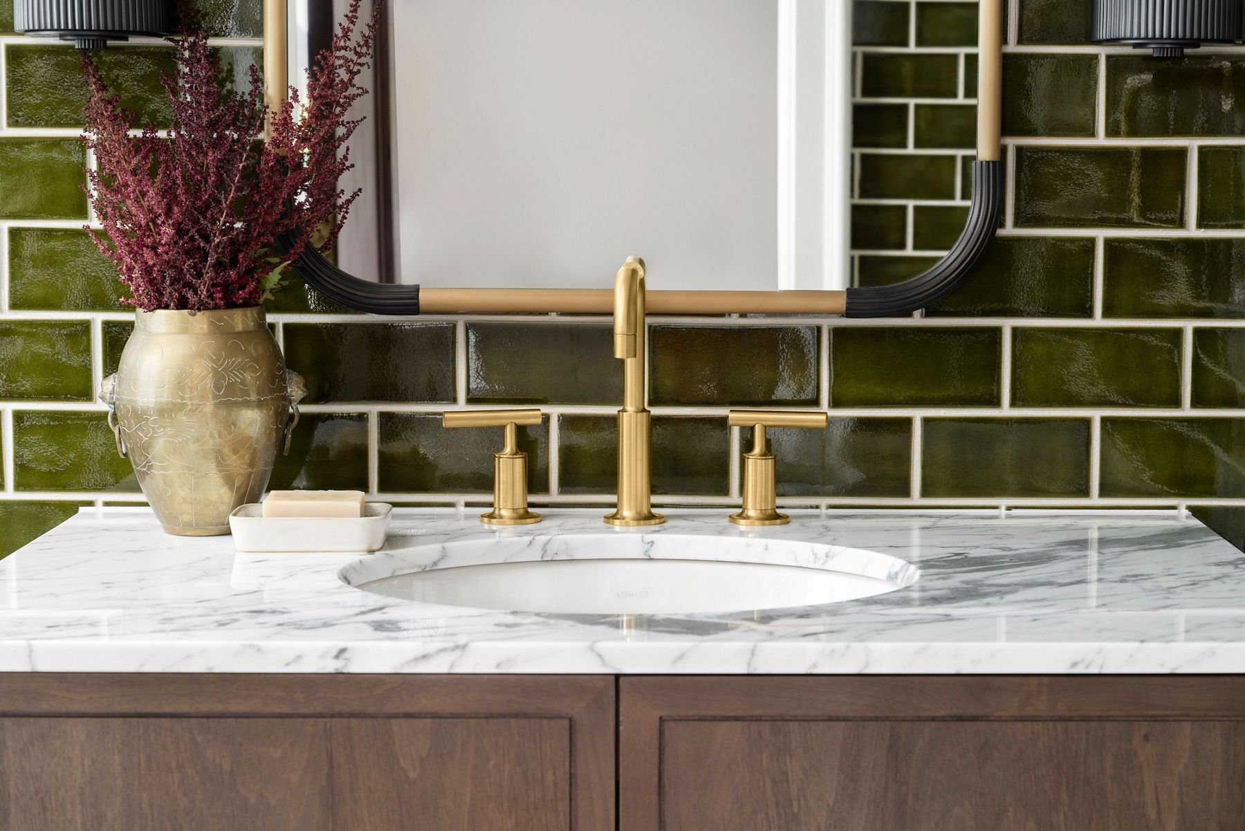 Kohler brushed brass bathroom faucets installed over modern subway tile backsplash.