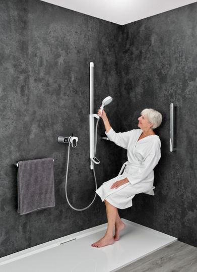 Older lady in a white dressing gown on a seat in a shower holdeing an accessible shower head