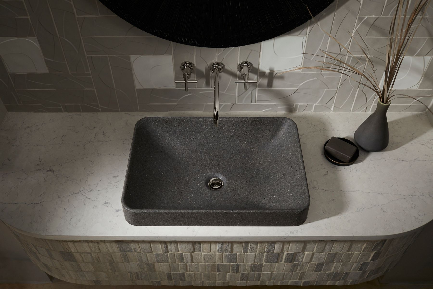 Black rectangular vessel sink with chrome faucet, gray countertop, and tiled backsplash.