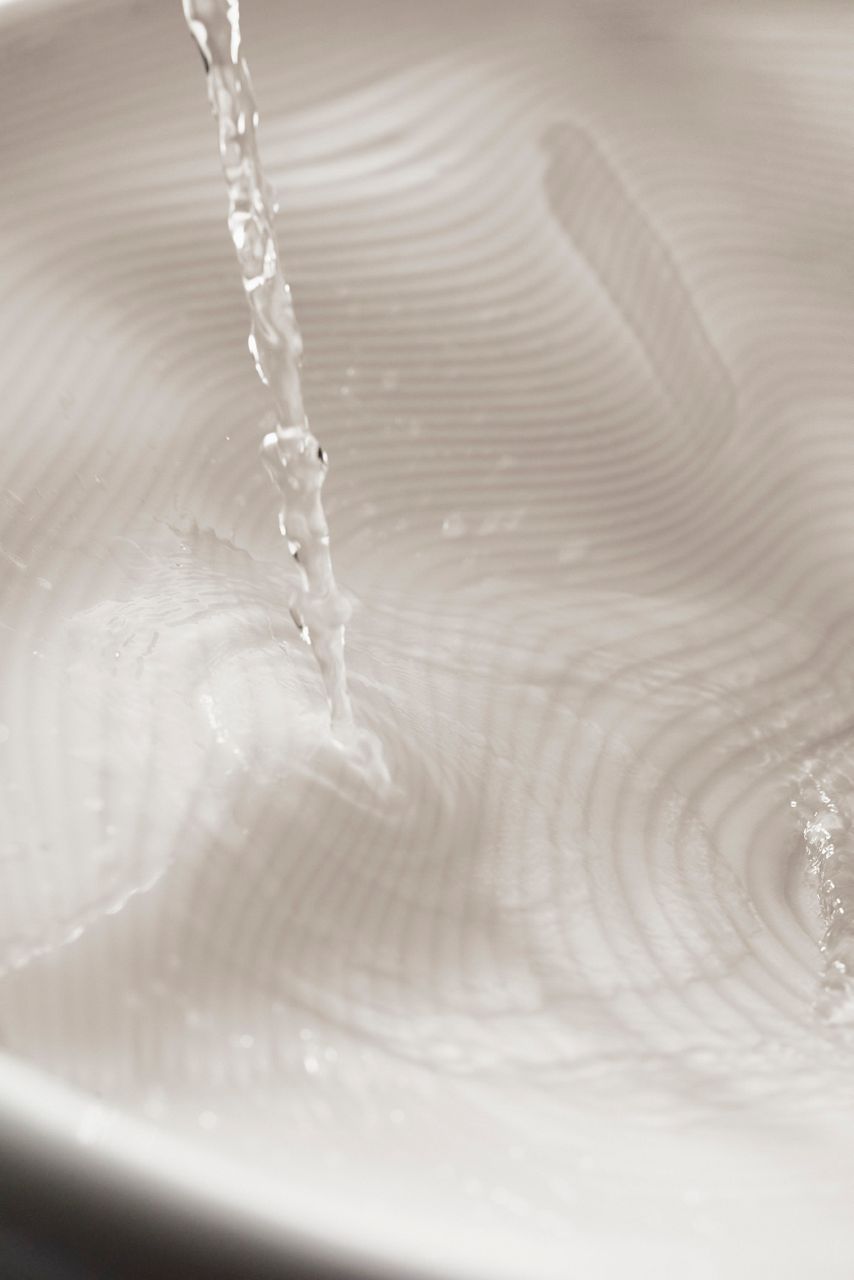 Close-up of water flowing into a white ceramic sink with 3D-printed pattern.