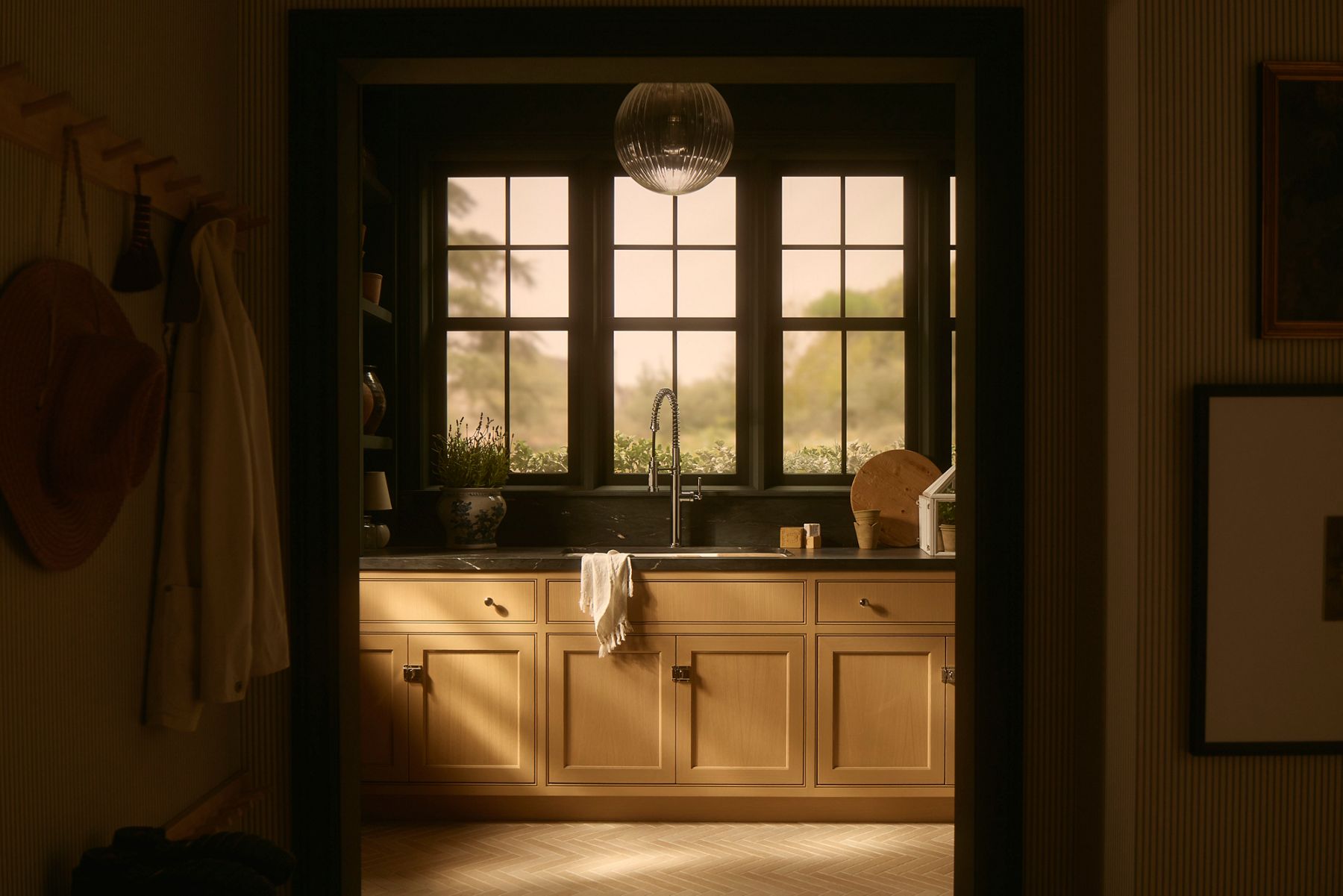 The Audrine sink in a mudroom designed with light wood cabinets, dark stone countertops, and a modern pendant light.