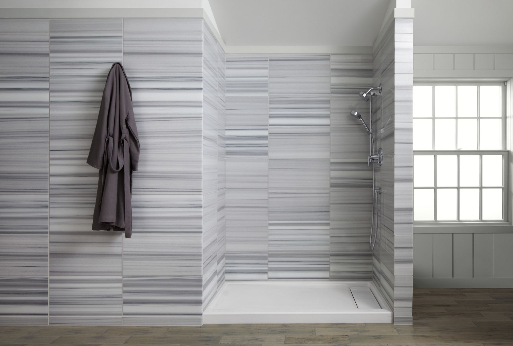 A shower area with a white base and multi-toned gray tile in very thin horizonal rectangles.