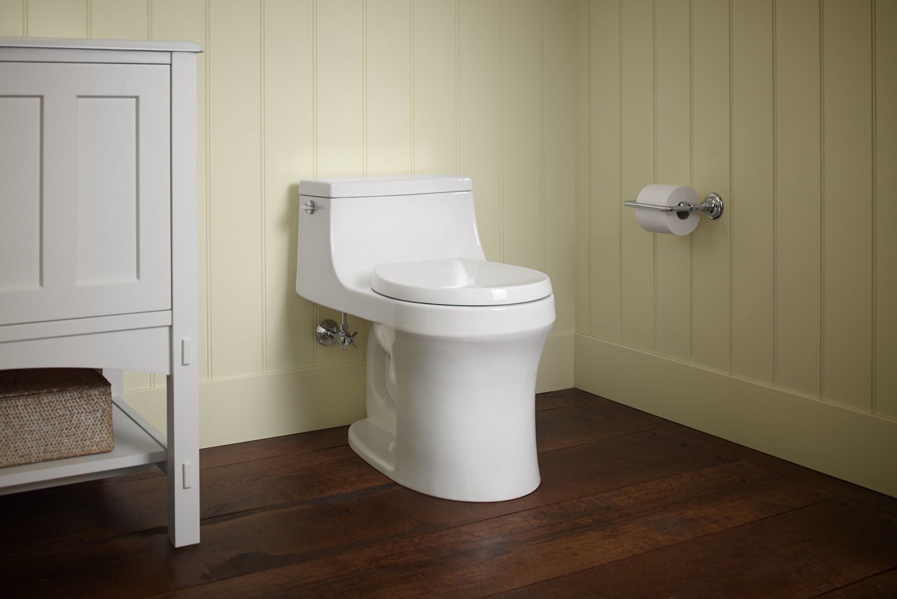 Floor-mounted white toilet attached to large base in bathroom with wood trim.