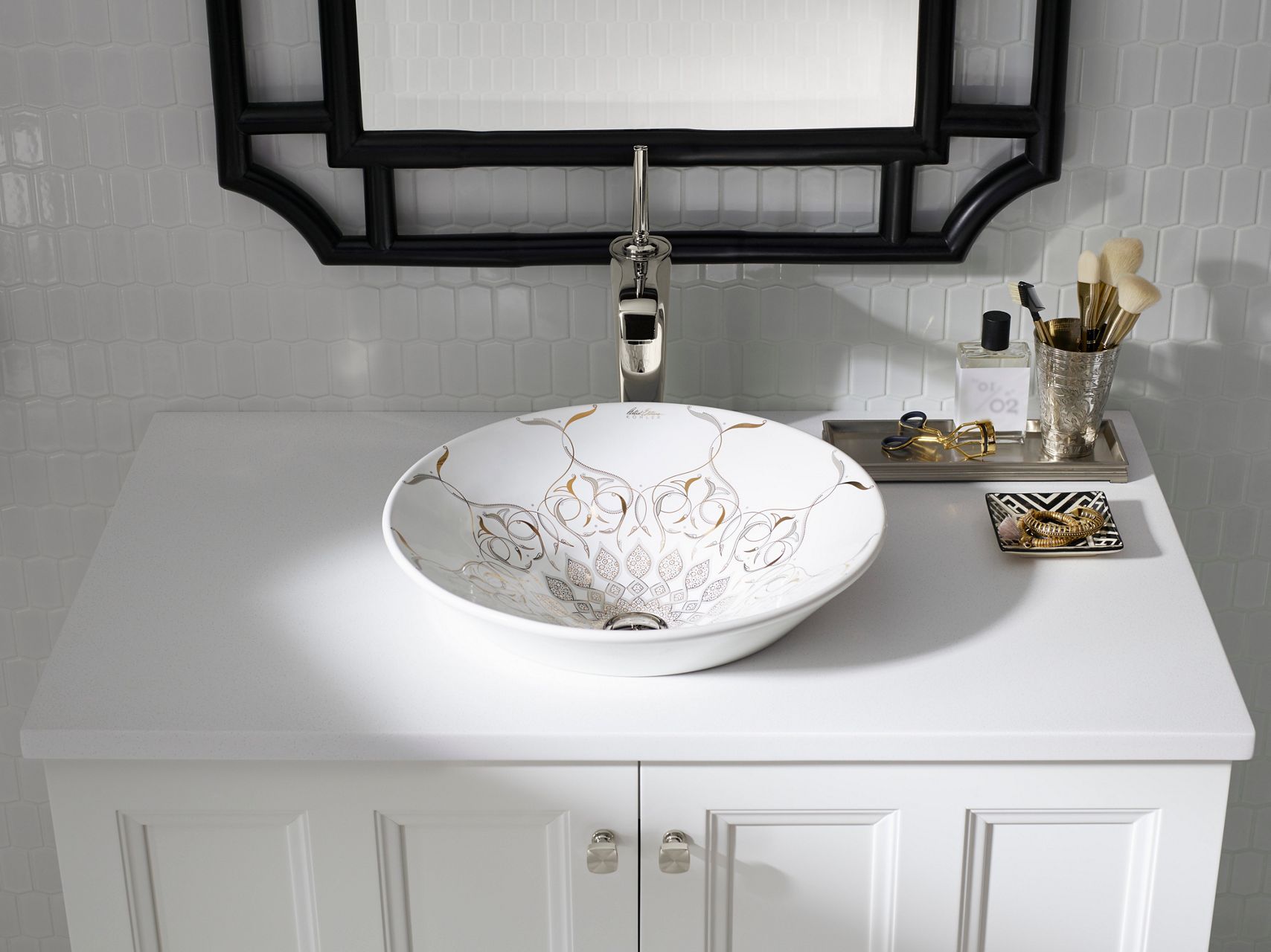 A close-up of a chrome bathroom sink faucet white bowl-style sink with decorative pattern on a white vanity, backed by a mirror and white tile