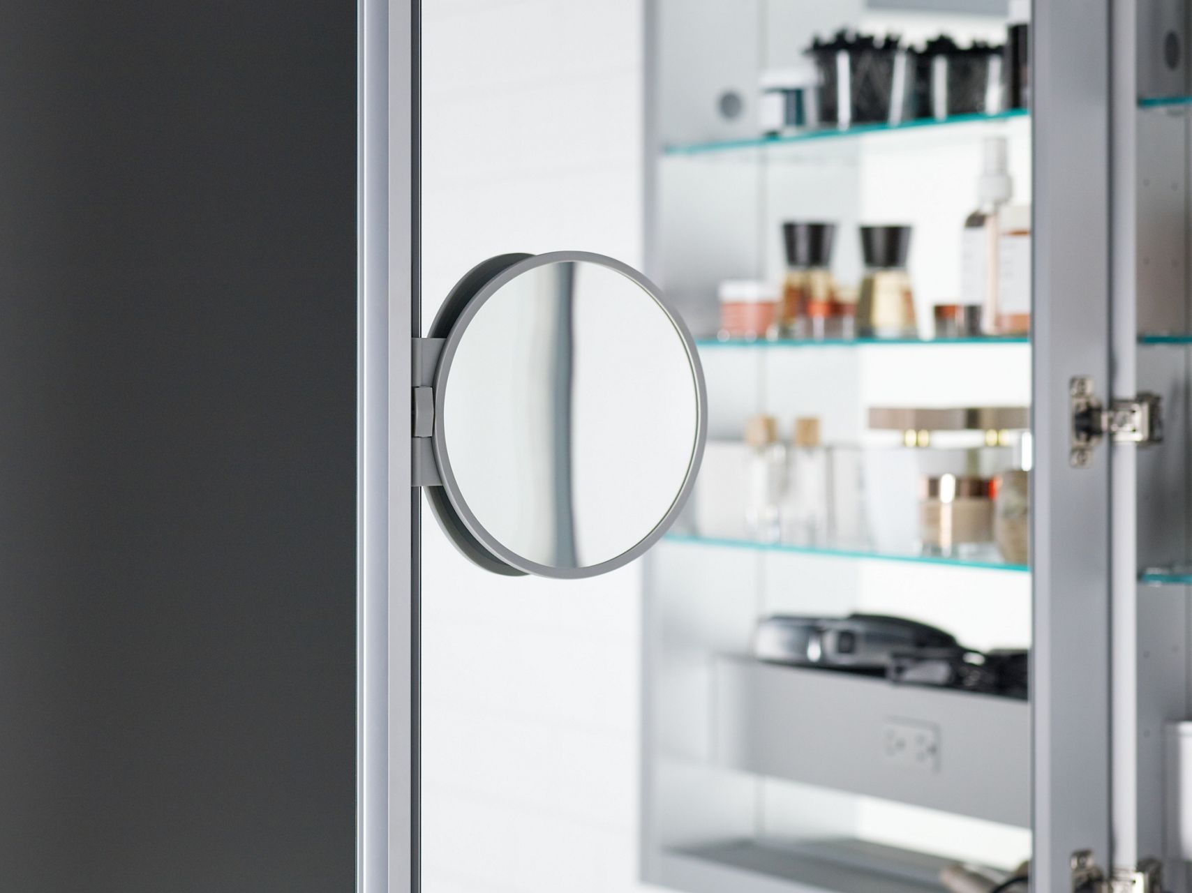Close-up detail of a fold-out magnification mirror connected to the interior door of a medicine cabinet.