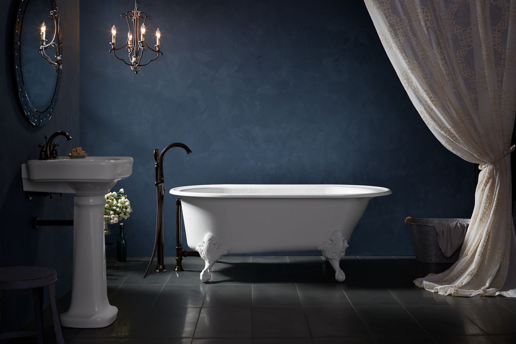 A white claw foot cast iron bath against a dark blue wall with a matte black bath filler at one end.