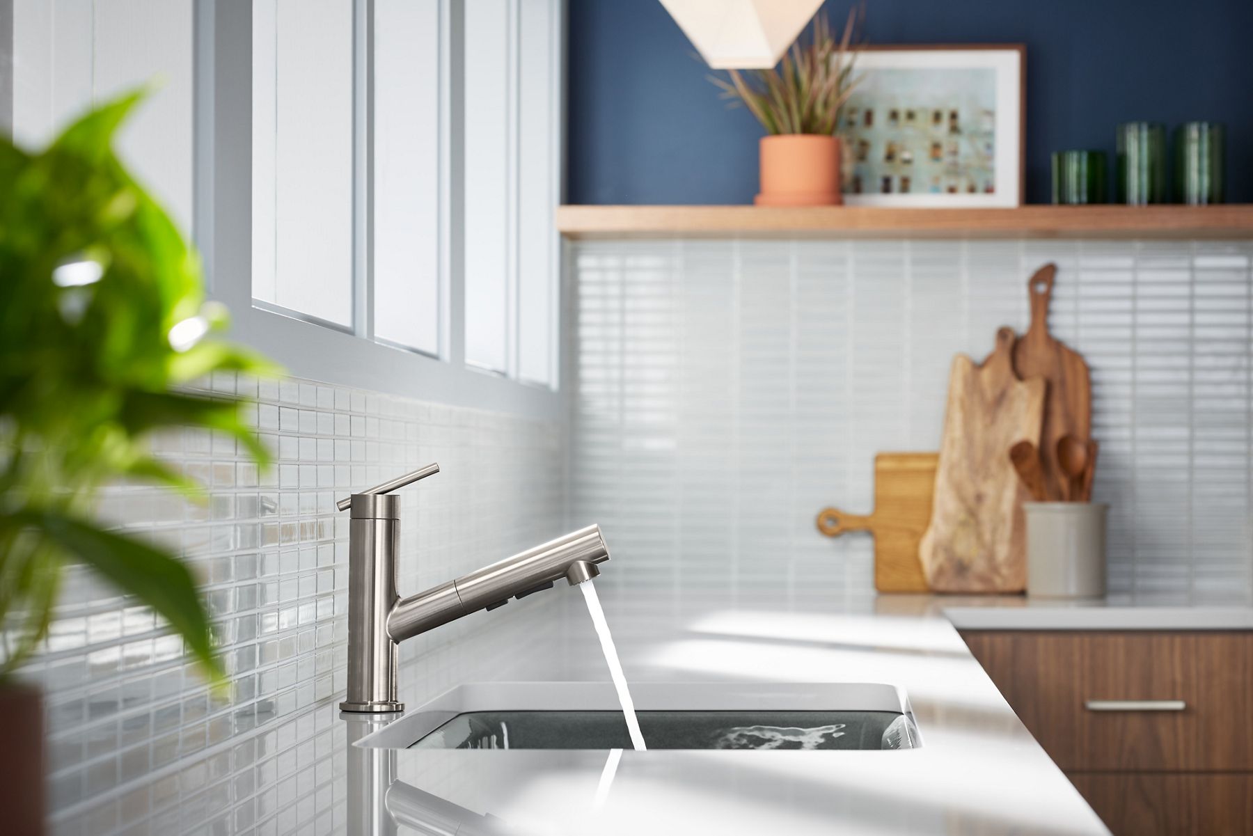 An angled close-up shot of a silver pull-out kitchen sink faucet. The faucet is attached to a white countertop in a sunlight space.