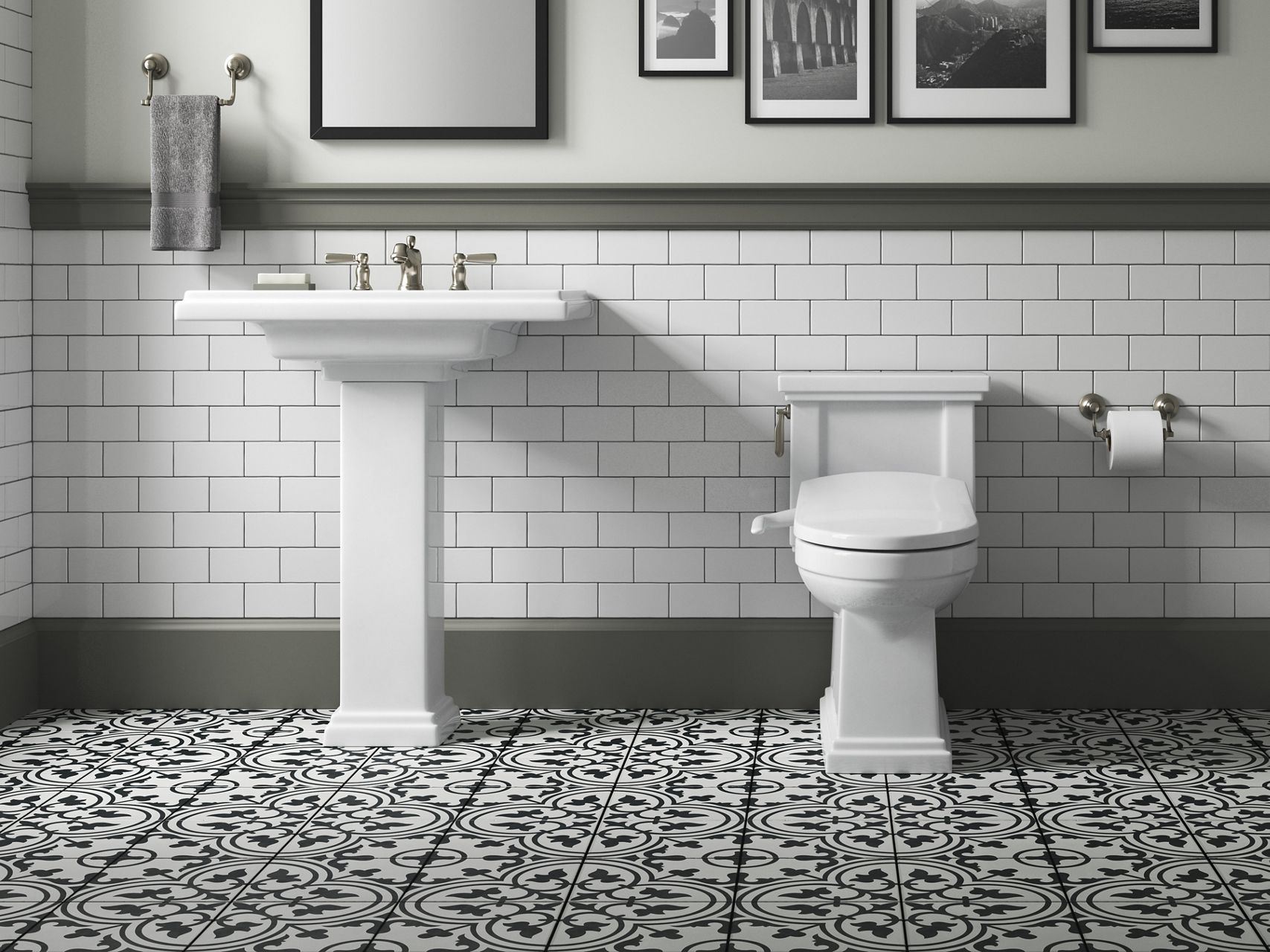 A white KOHLER Tresham pedestal sink in a bathroom with white subway tile walls, gray bullnose trim, and black and white patterned floor tile.