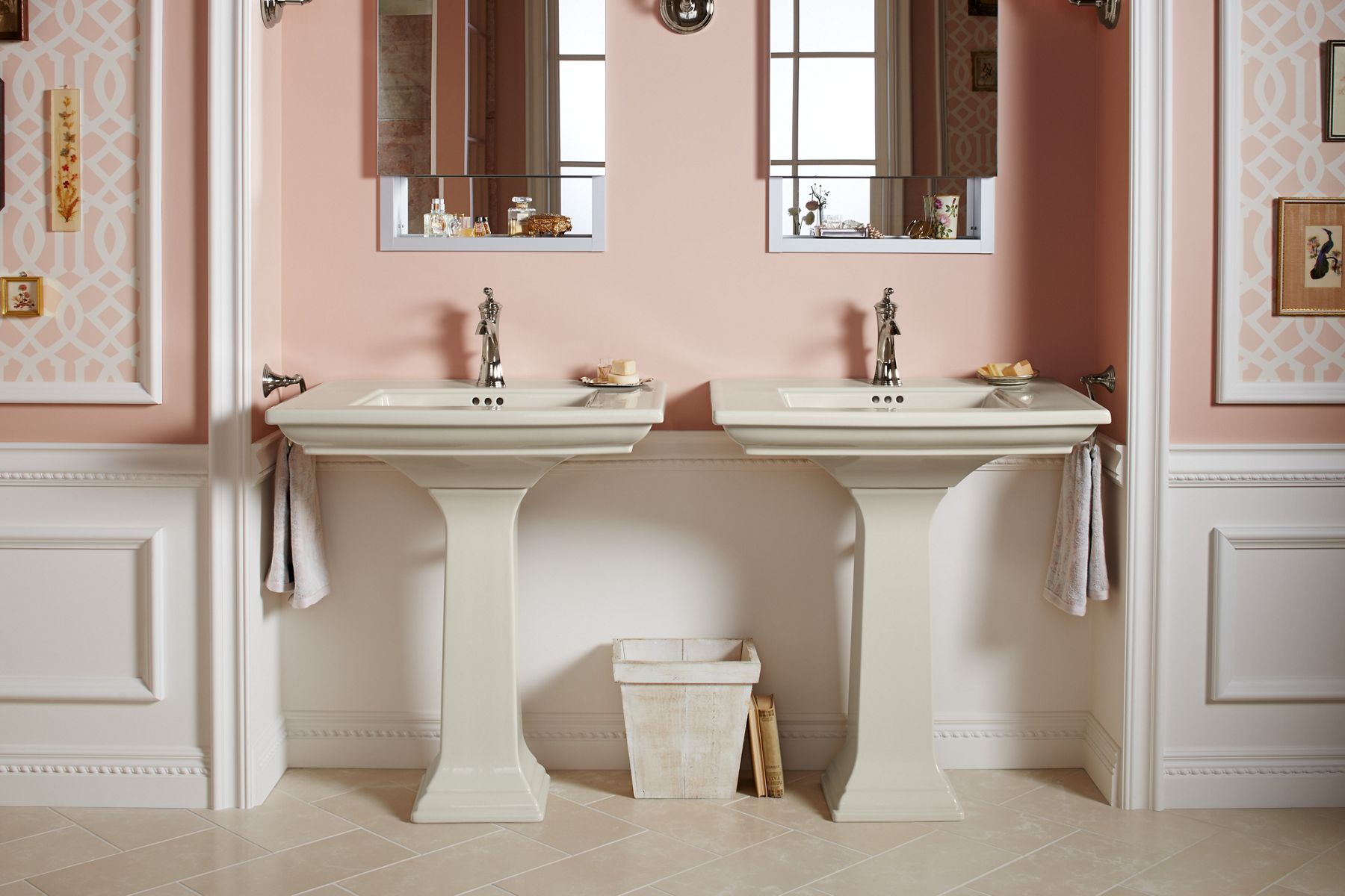 Front view of a Memoirs Stately pedestal sink in a Biscuit color against a pink bathroom wall with white lower paneling.