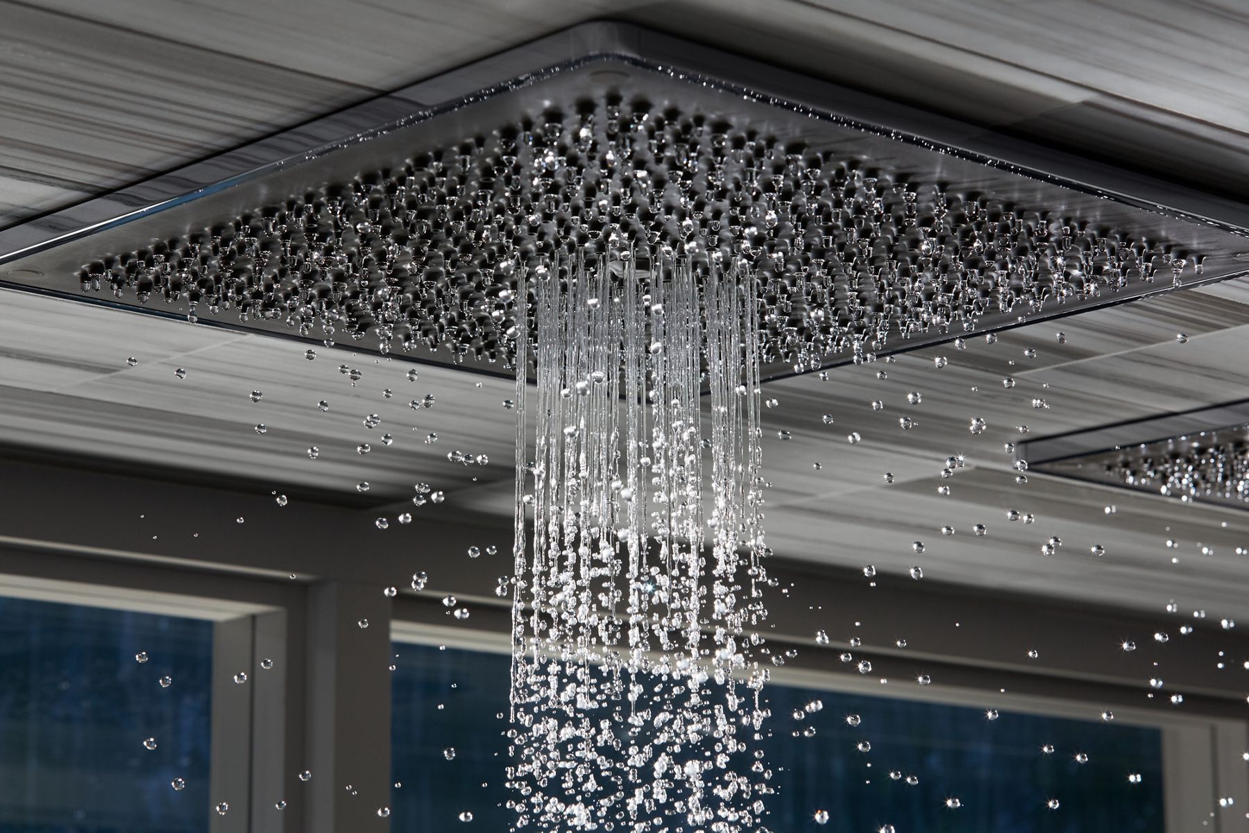 Close-up of water flowing from a KOHLER rainhead mounted on the ceiling of a shower.