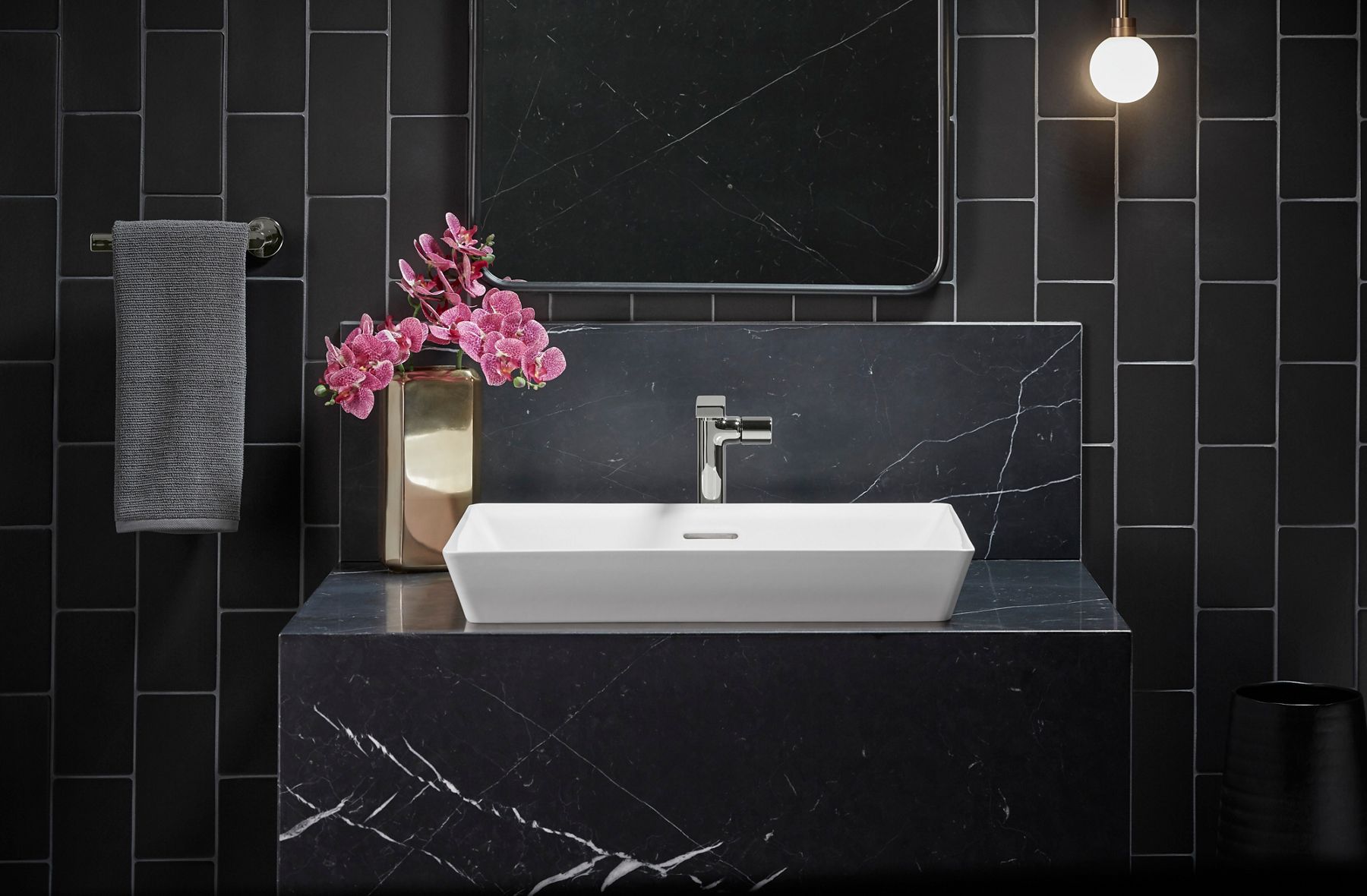 A white rectangular vessel sink on a gray counter with a gray stone wall behind it and a chrome faucet.