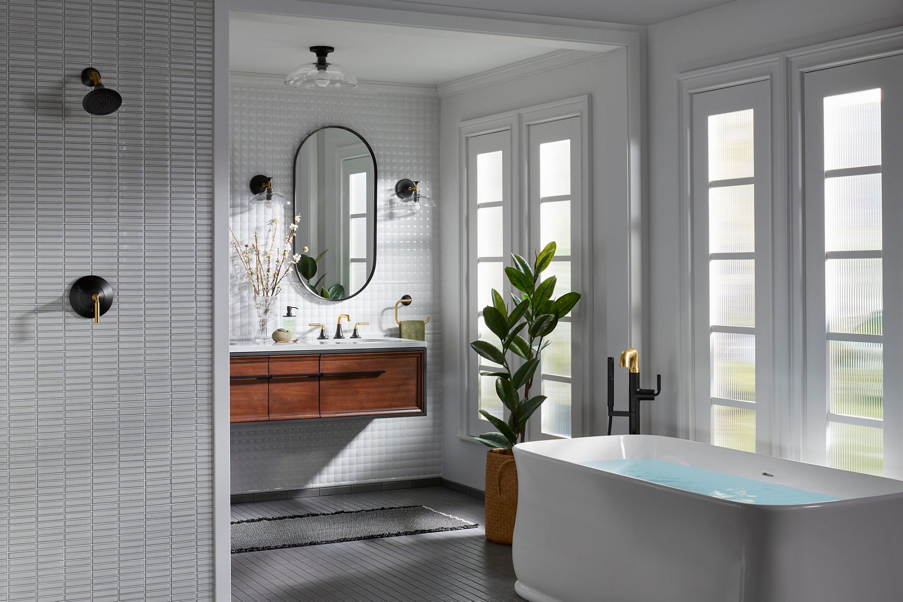 Une salle de bain dans des tons de blanc, avec des grains de bois naturels, une plante verte et des produits de la collection Tone dans un fini bicolore noir mat et laiton brossé.