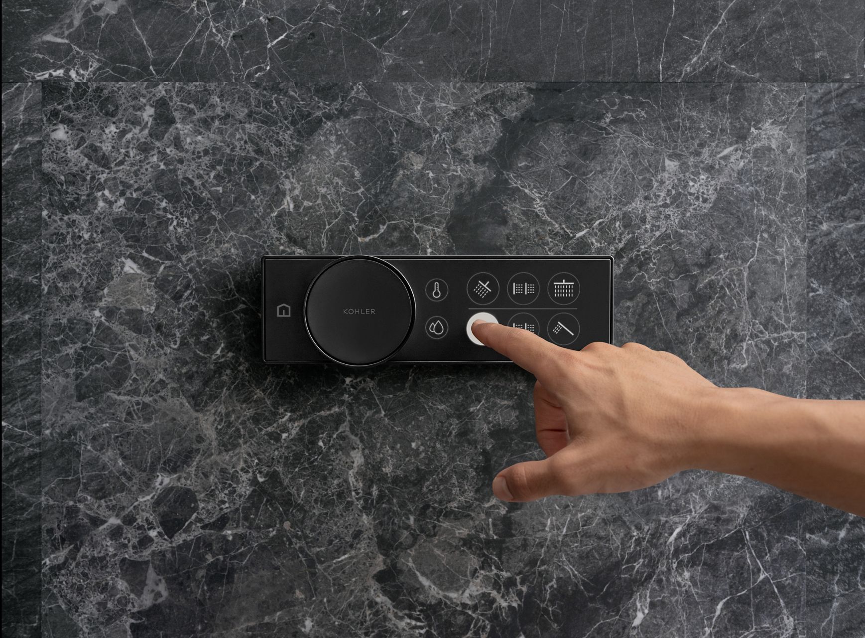 A person switches shower outlets using a black KOHLER Anthem digital shower control mounted on a black marble wall.