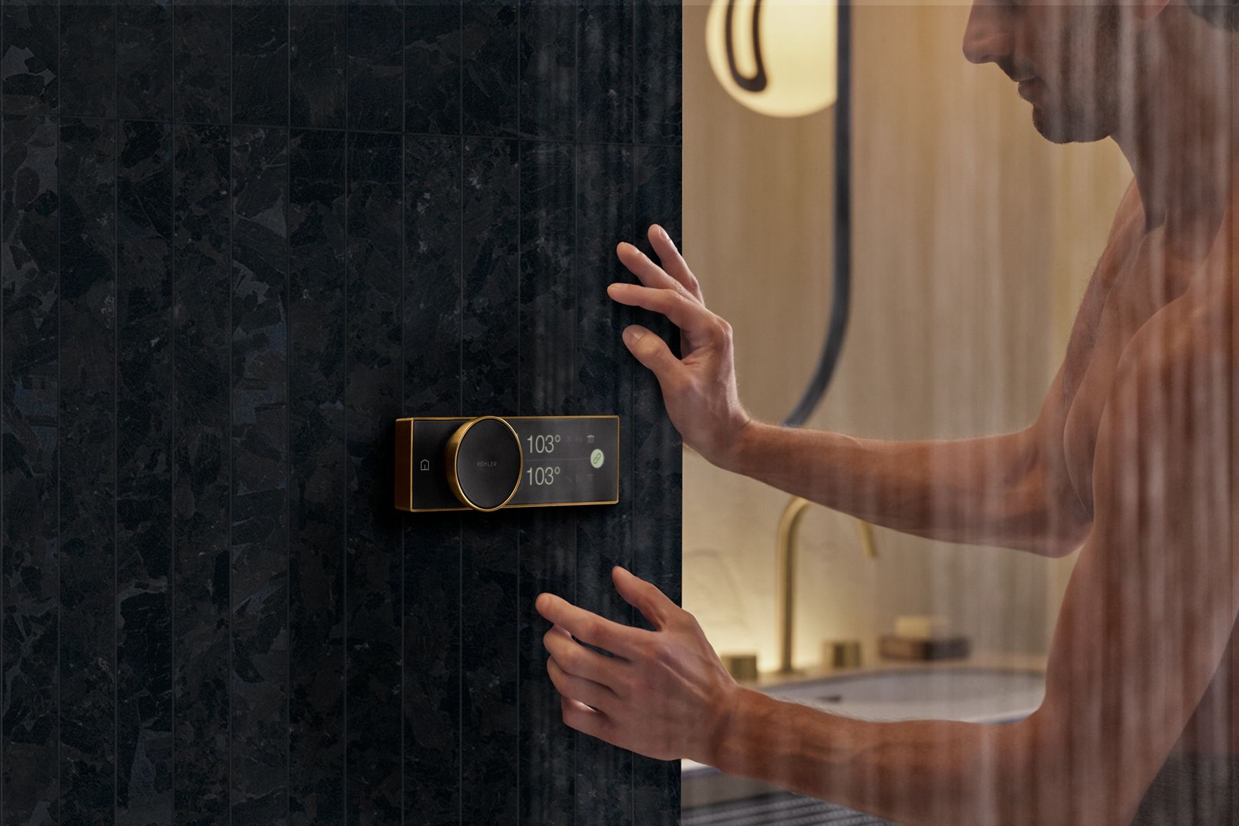 Un homme tend la main pour toucher le panneau de commande Anthem noir et laiton contre un mur de pierre gris foncé.