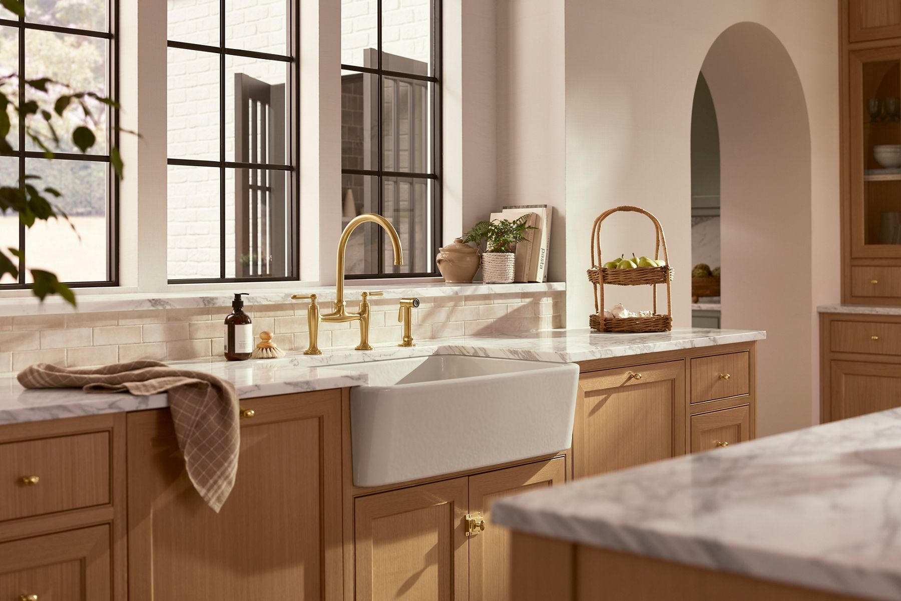 Un dessus de meuble-lavabo pour salle de bain avec un robinet de salle de bain Casita Kohler au fini doré et des poignées à levier, avec d’autres accessoires de meuble-lavabo en arrière-plan
