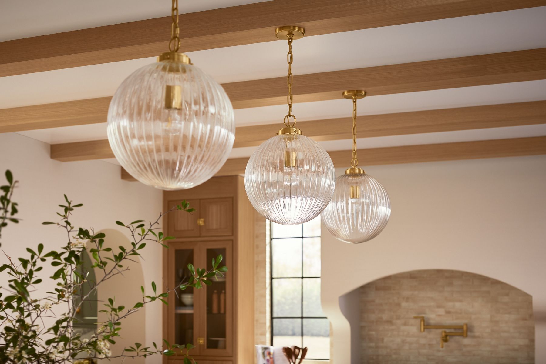 Three pendent lights installed above a kitchen counter in vibrant modern brass finish