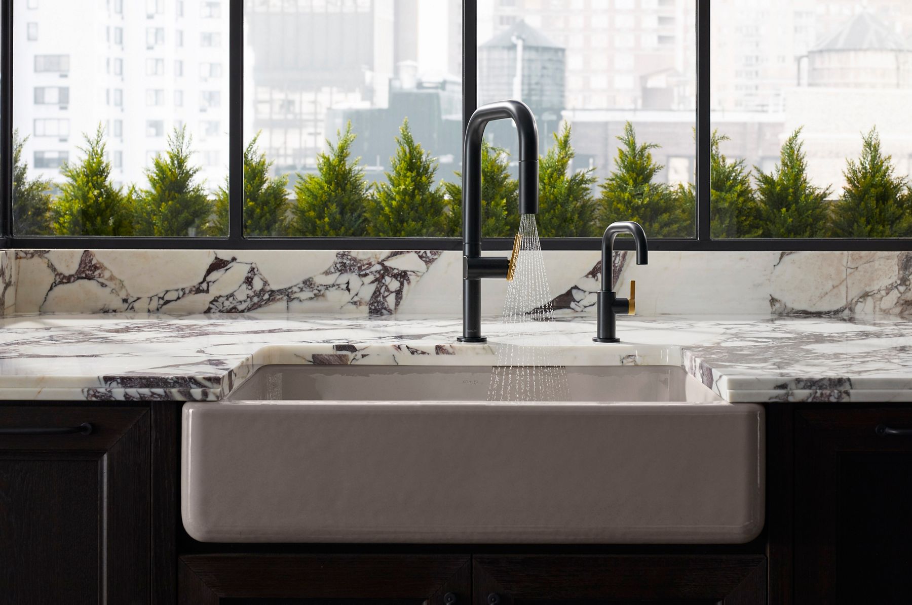 Modern kitchen with marble countertops featuring two black faucets with sleek designs. A large window with a view of greenery is in the background.