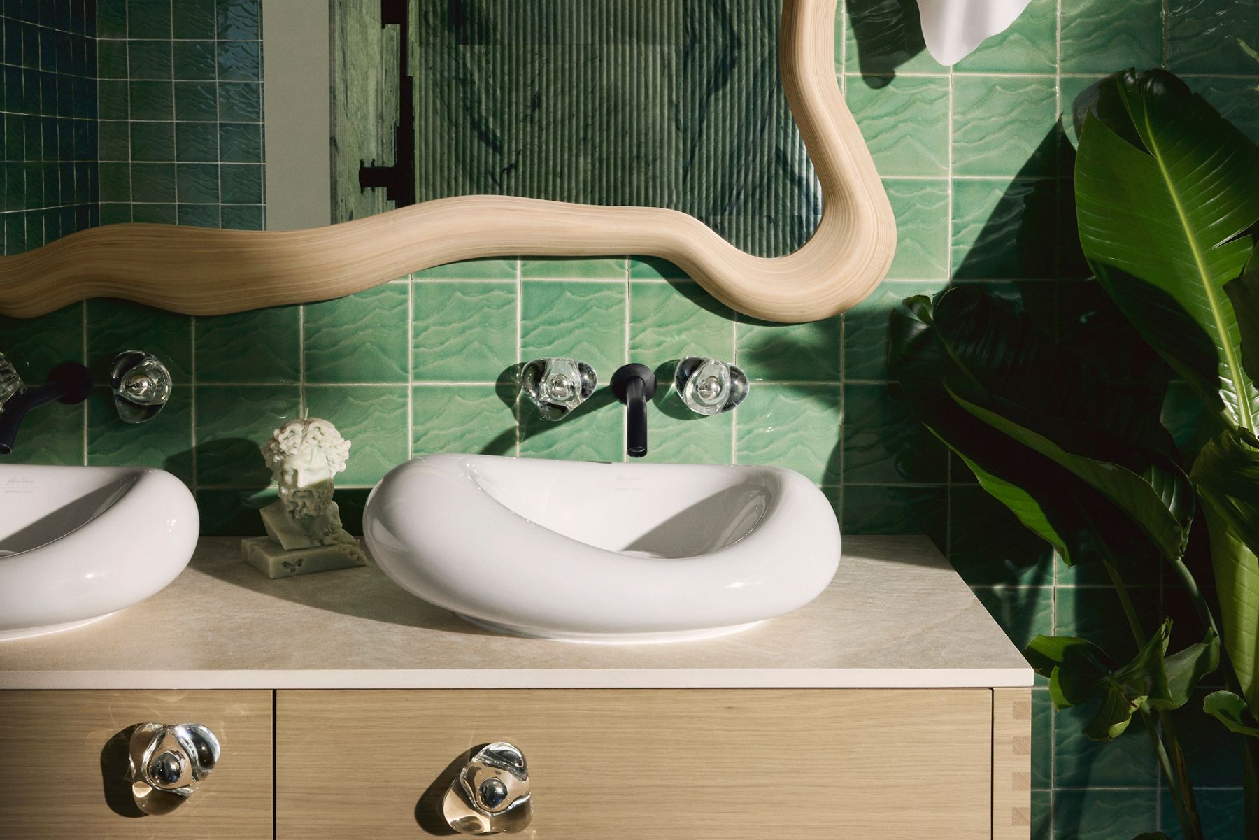 Salle de bain moderne avec deux lavabos en surface blancs, un miroir en bois ondulé et un mur carrelé vert clair.