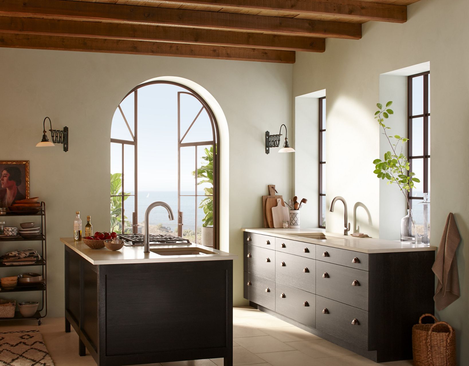 A large open and sunny kitchen, with exposed wooden ceiling beams and an arched window, bring focus to the center island adorned with Sensate touchless faucet and Riverby undermount sink.