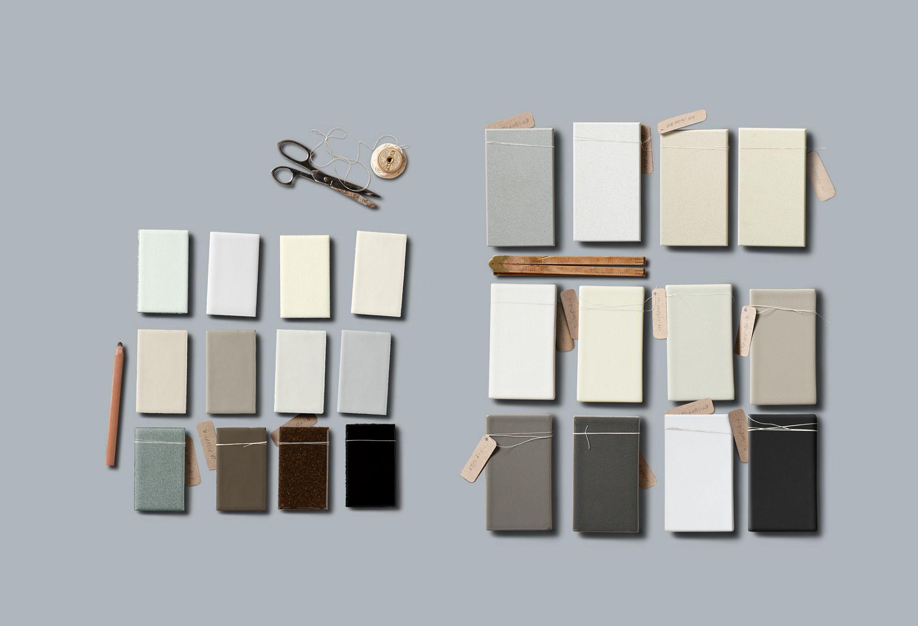 A cup of coffee sits on a round white table among white and gray tile and finish samples, design plans, a notebook, and an iPad with a room design visible on the screen.