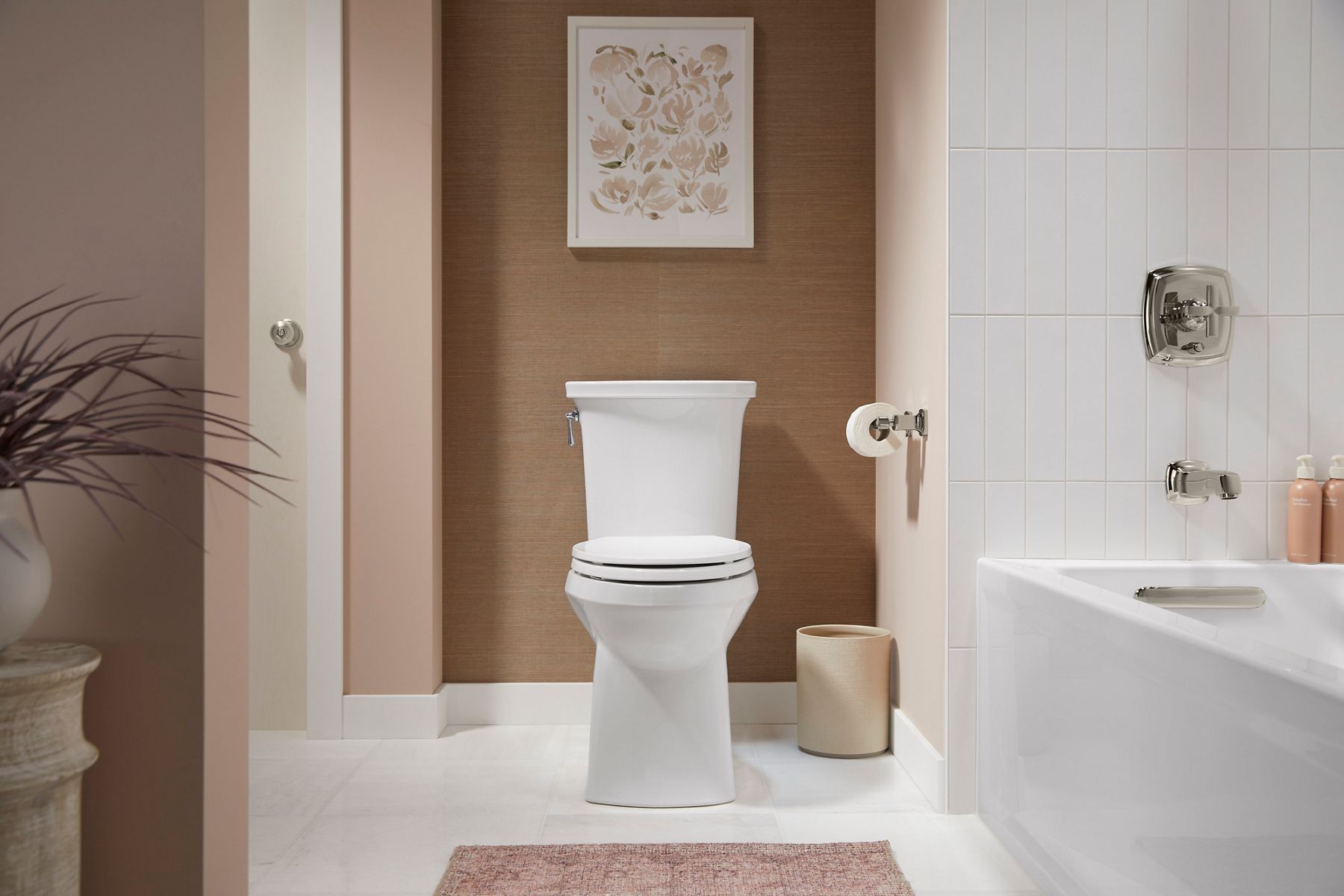 White Kohler Toilet in bathroom with brown walls, sitting next to a Kohler bathtub with vertical white subway tile.