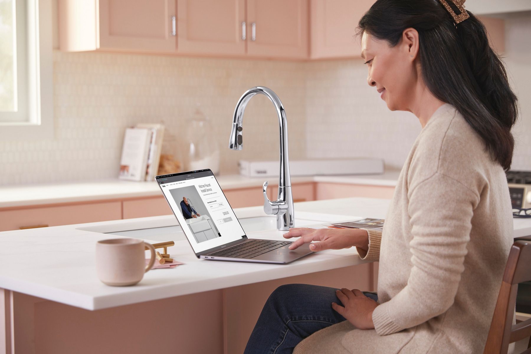 A person sitting at a kitchen island with their laptop computer open to a page about Kohler support services.