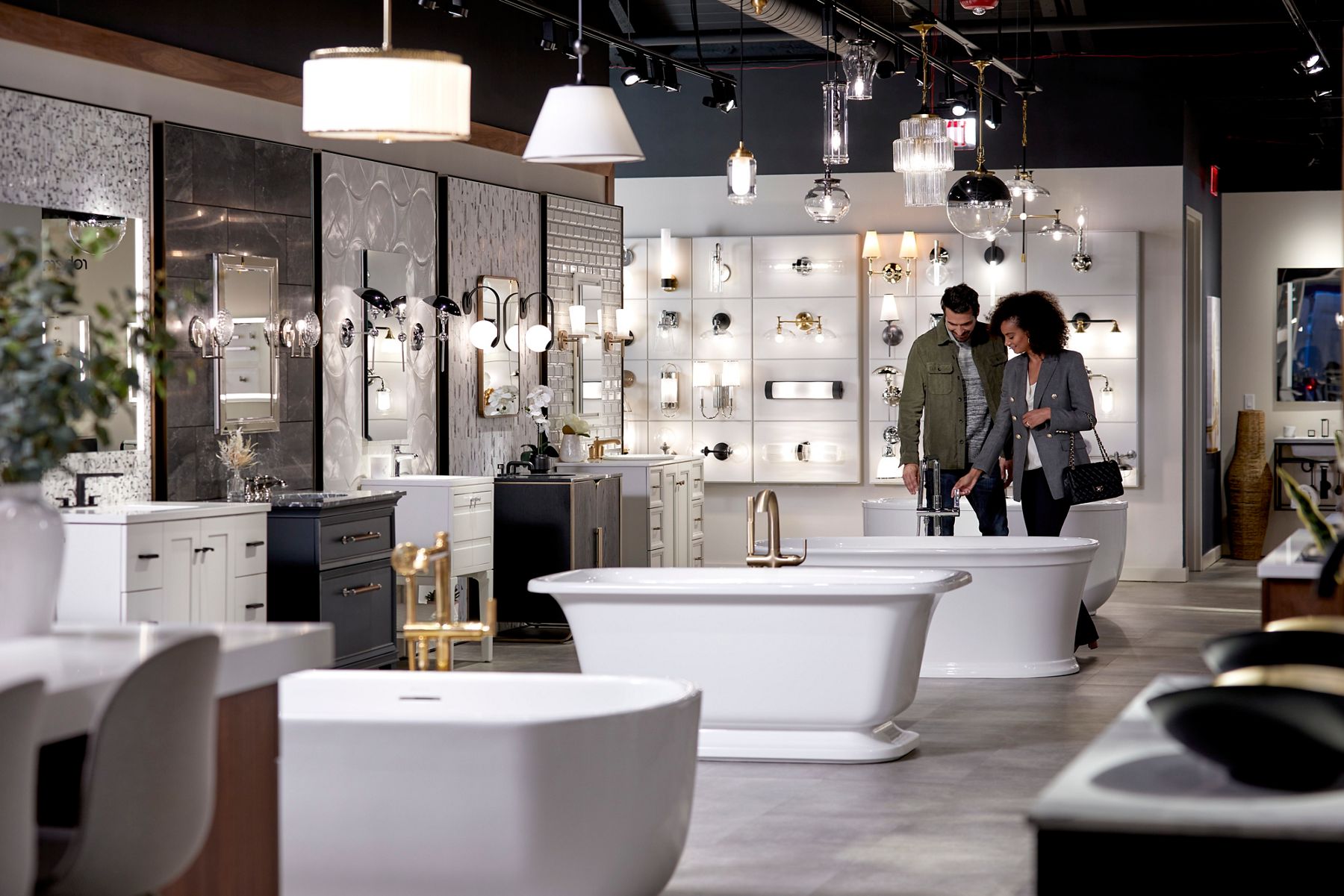 Wide image of a couple shopping inside of a bright and open Kohler store, looking at and touching the faucet on a Kohler freestanding bathtub.