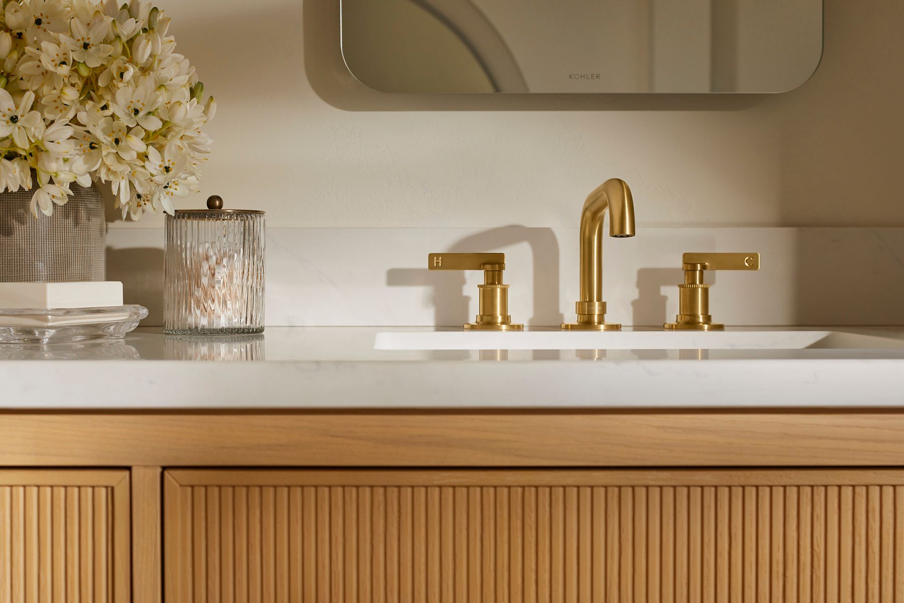 Bathroom vanity with brass faucet set and white countertop decorated with flowers and accessories.