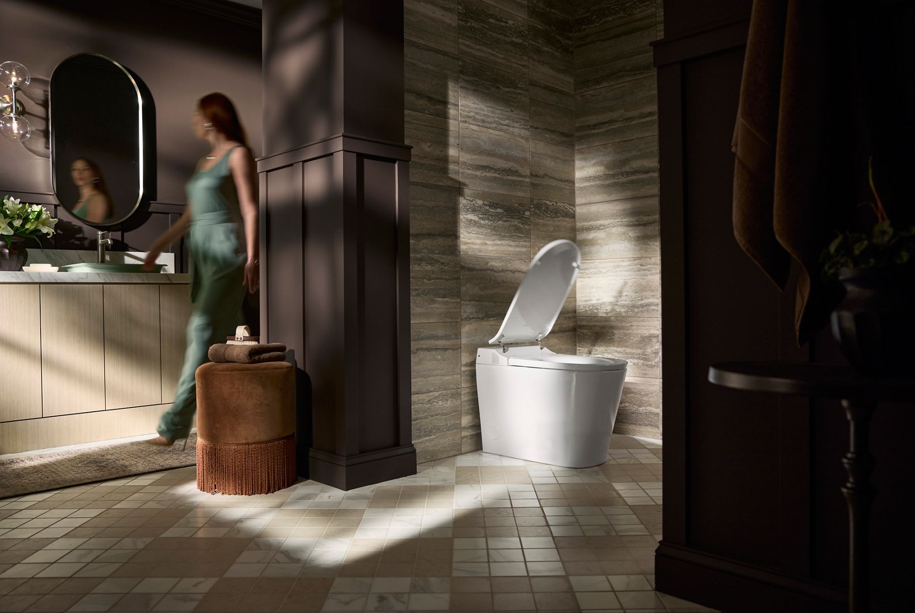 Modern bathroom interior with a woman walking past a smart toilet and vanity mirror. 