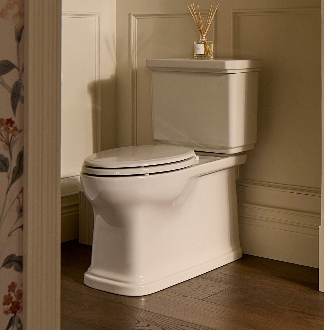 Two-piece toilet with a rectangular tank and and elongated bowl, placed against a paneled bathroom wall with a diffuser on top of the tank.